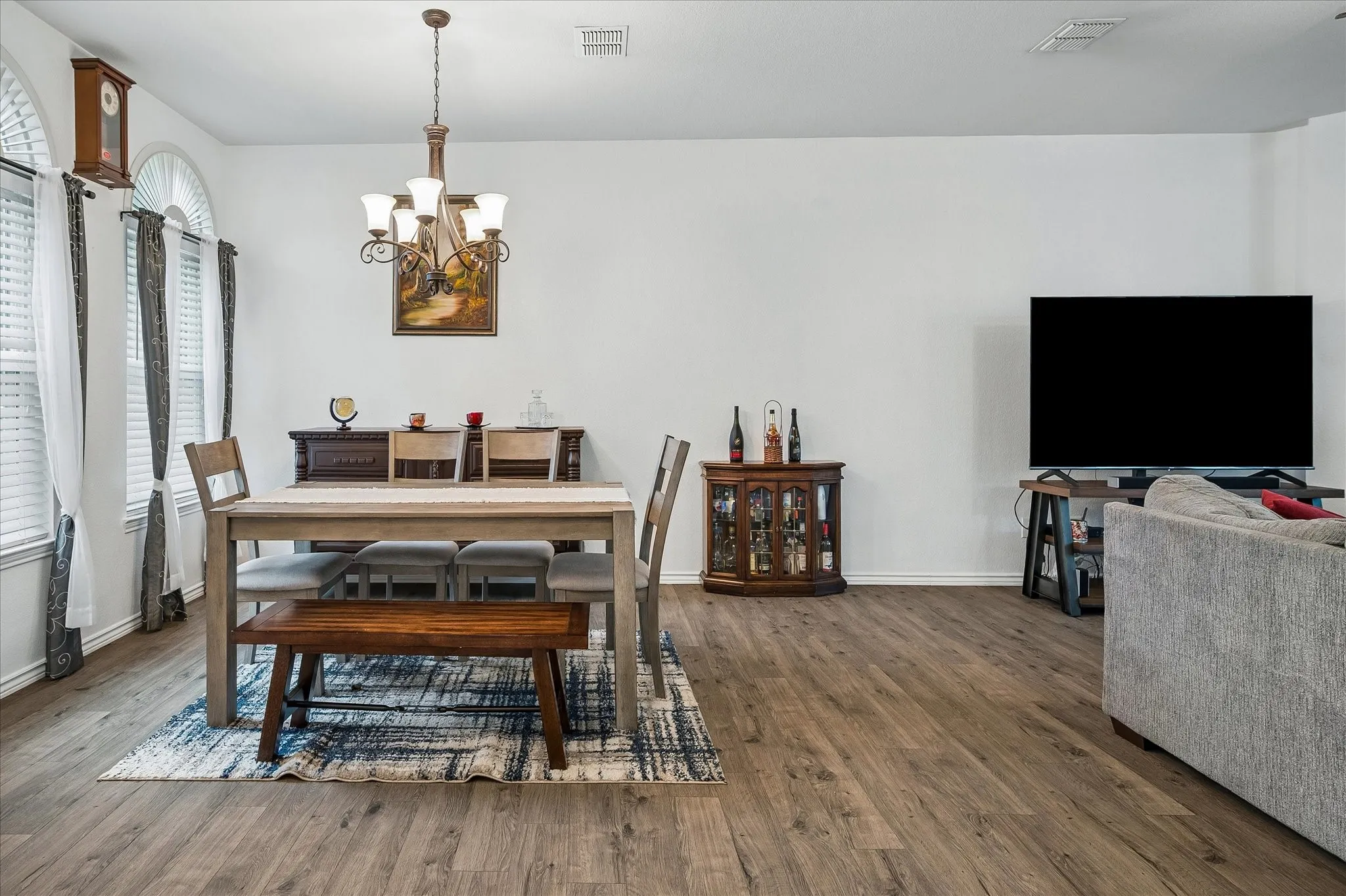 Wood-finish flooring, arched windows with blinds, and a five-light chandelier