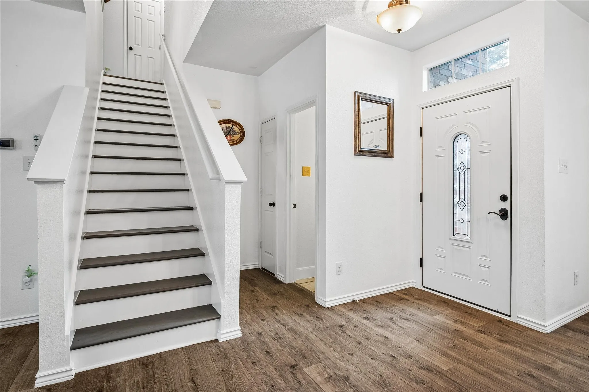 Entryway featuring wood-finish flooring, a white front door with decorative glass, and a transom window