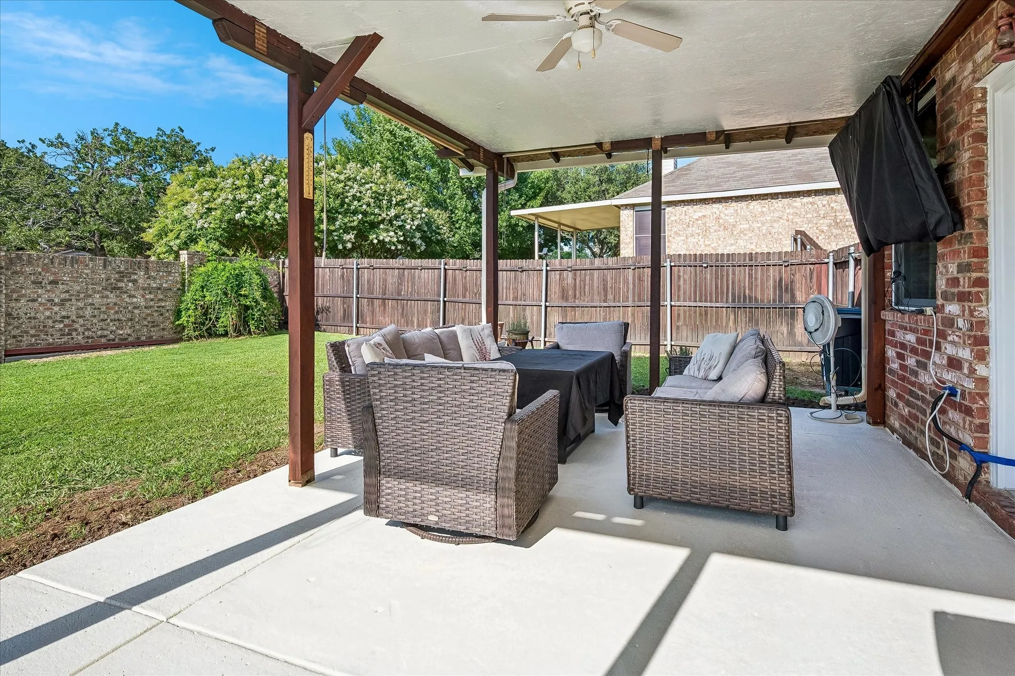 Covered patio with a ceiling fan, concrete flooring, and a brick exterior wall