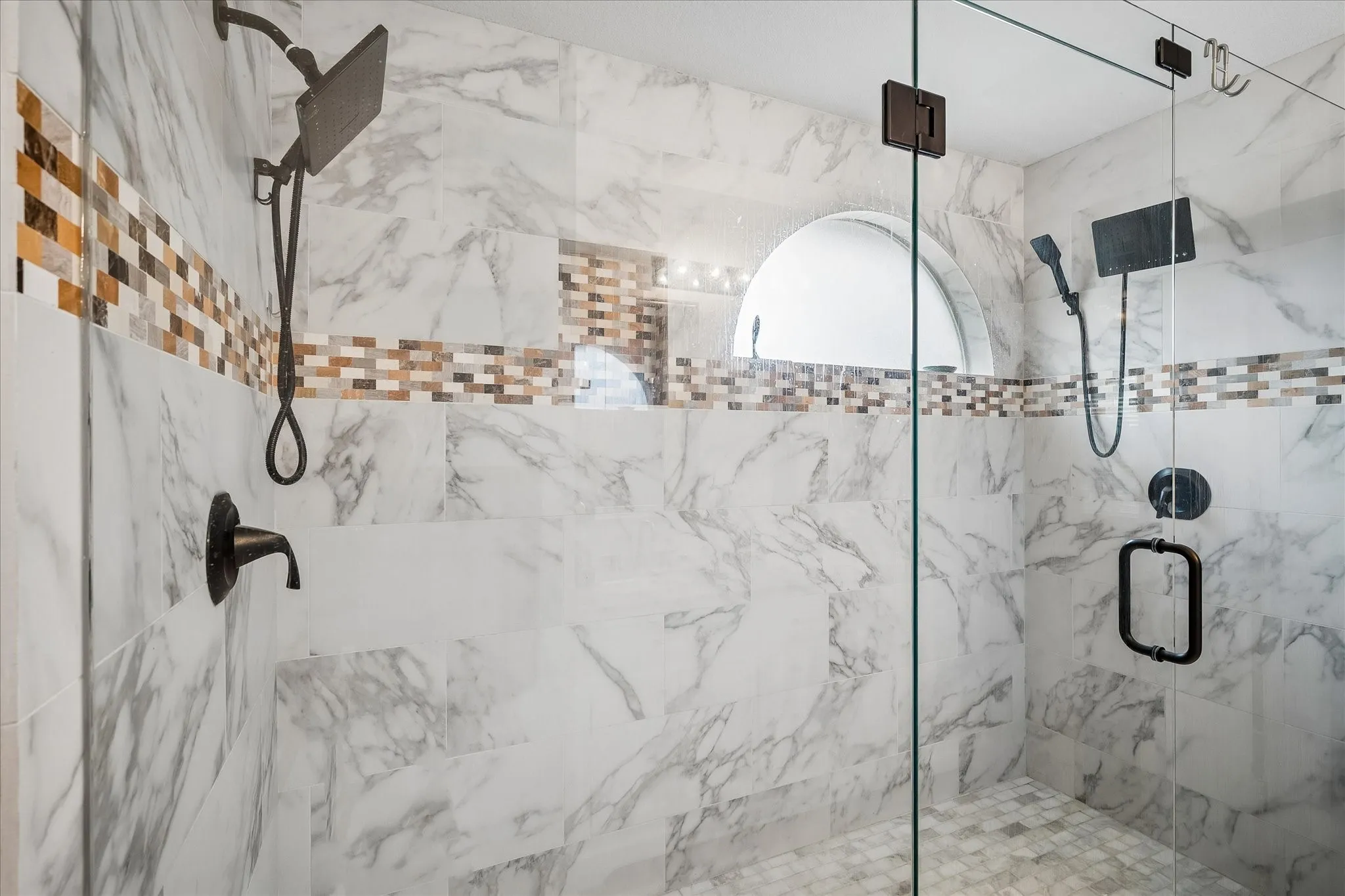 Tiled shower with glass enclosure, dual shower heads, and an arched window