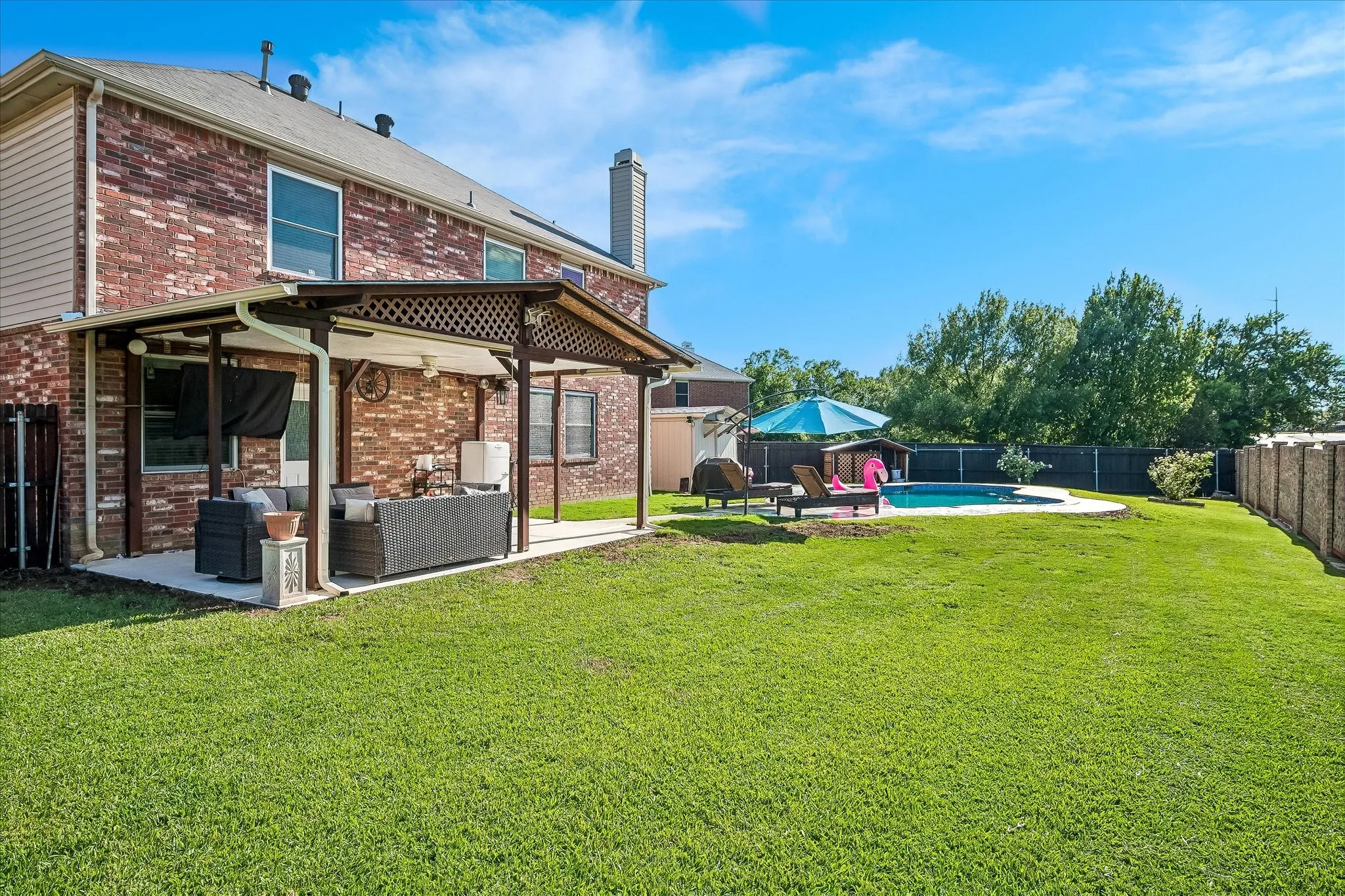 Brick exterior home with a covered patio, an in-ground swimming pool, and a fenced backyard with a manicured lawn