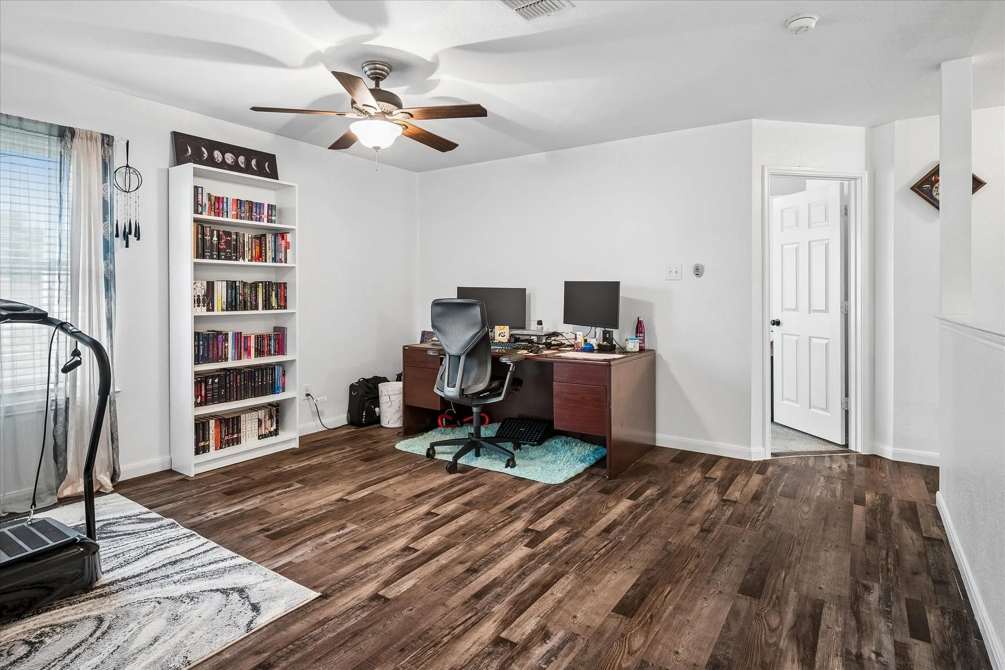 Wood-finish flooring, ceiling fan, white paneled door, and a built-in shelving unit