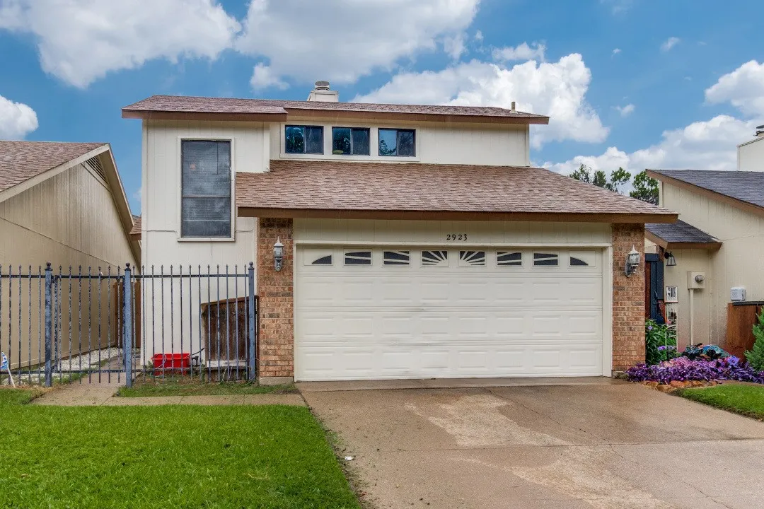 Two-story residence featuring a two-car garage with transom windows, brick accents, and a front yard with purple landscaping