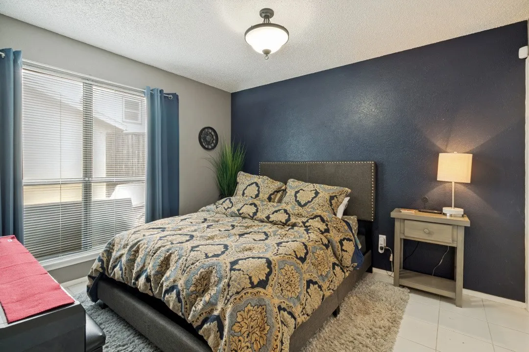 Room featuring a large window with blinds, a prominent dark accent wall, and a ceiling-mounted light fixture