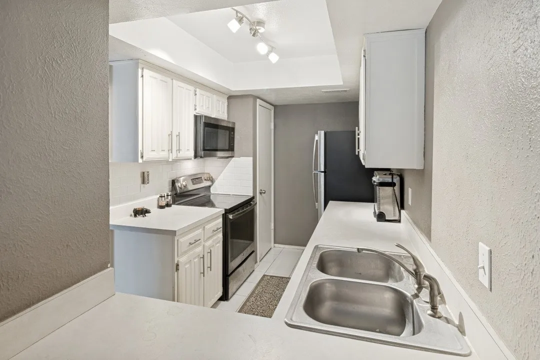 Compact kitchen featuring white cabinetry, a stainless steel double-basin sink, and a black and stainless steel appliance package