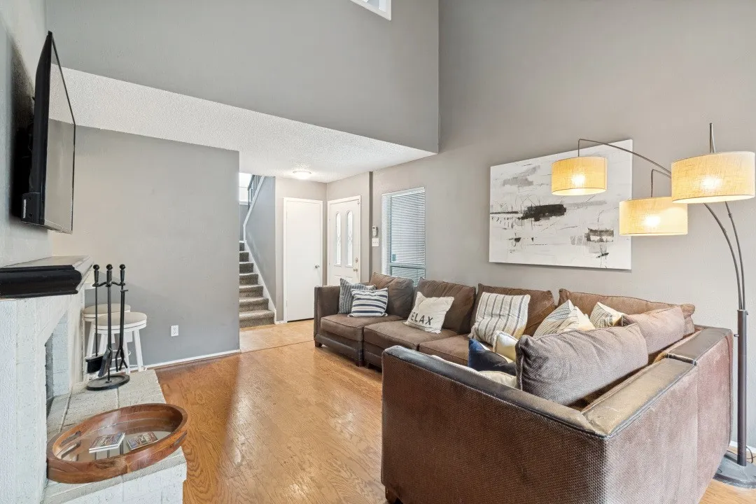 Living room featuring wood-finish flooring, a white-painted fireplace with a black mantel, and a multi-level ceiling