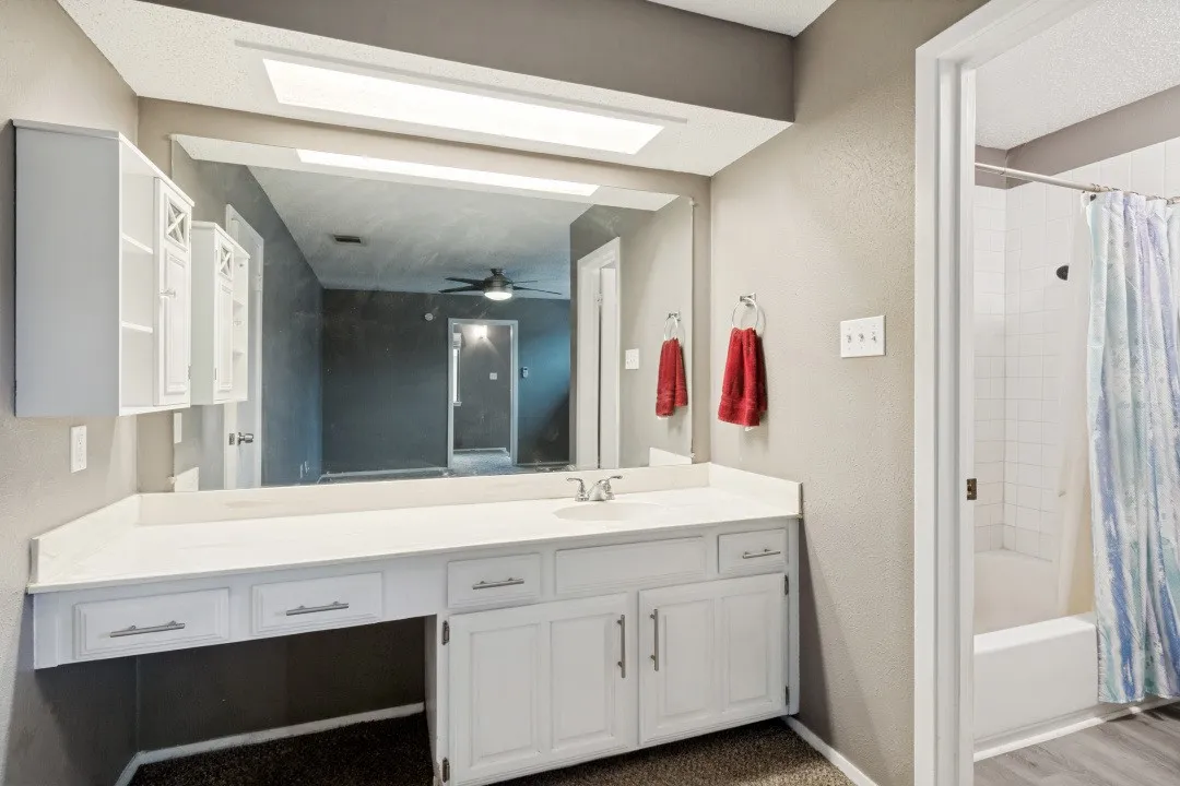 Bathroom vanity with white cabinetry, a single basin sink, and an expansive mirror