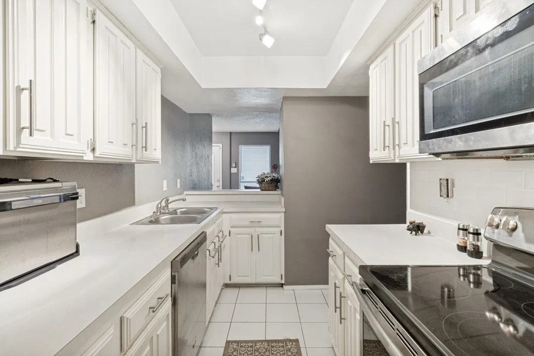Galley kitchen with white shaker-style cabinetry, white countertops, and white tile flooring