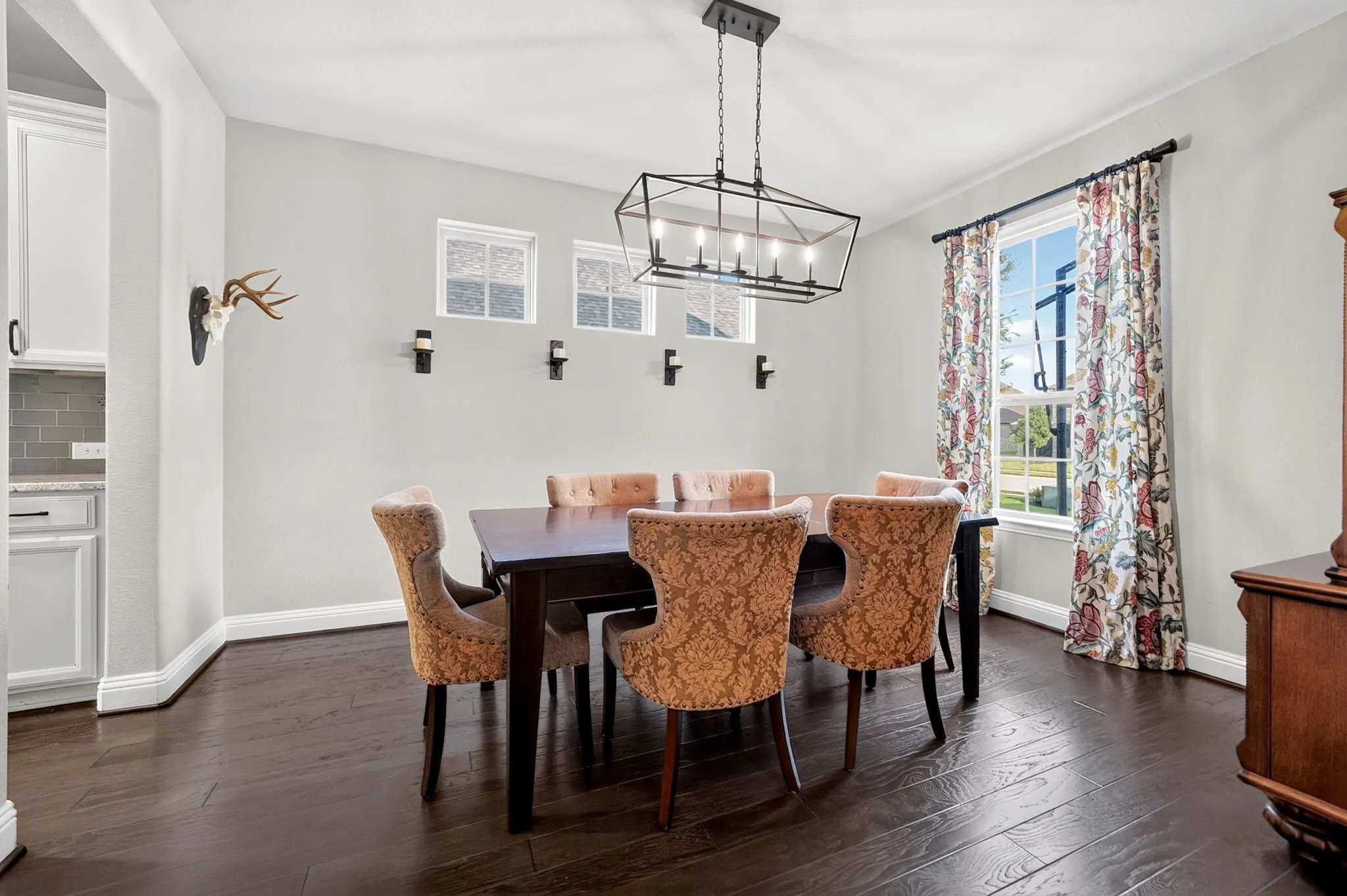 Dining area featuring dark wood-finish flooring, a contemporary black metal chandelier, and a large window with white trim