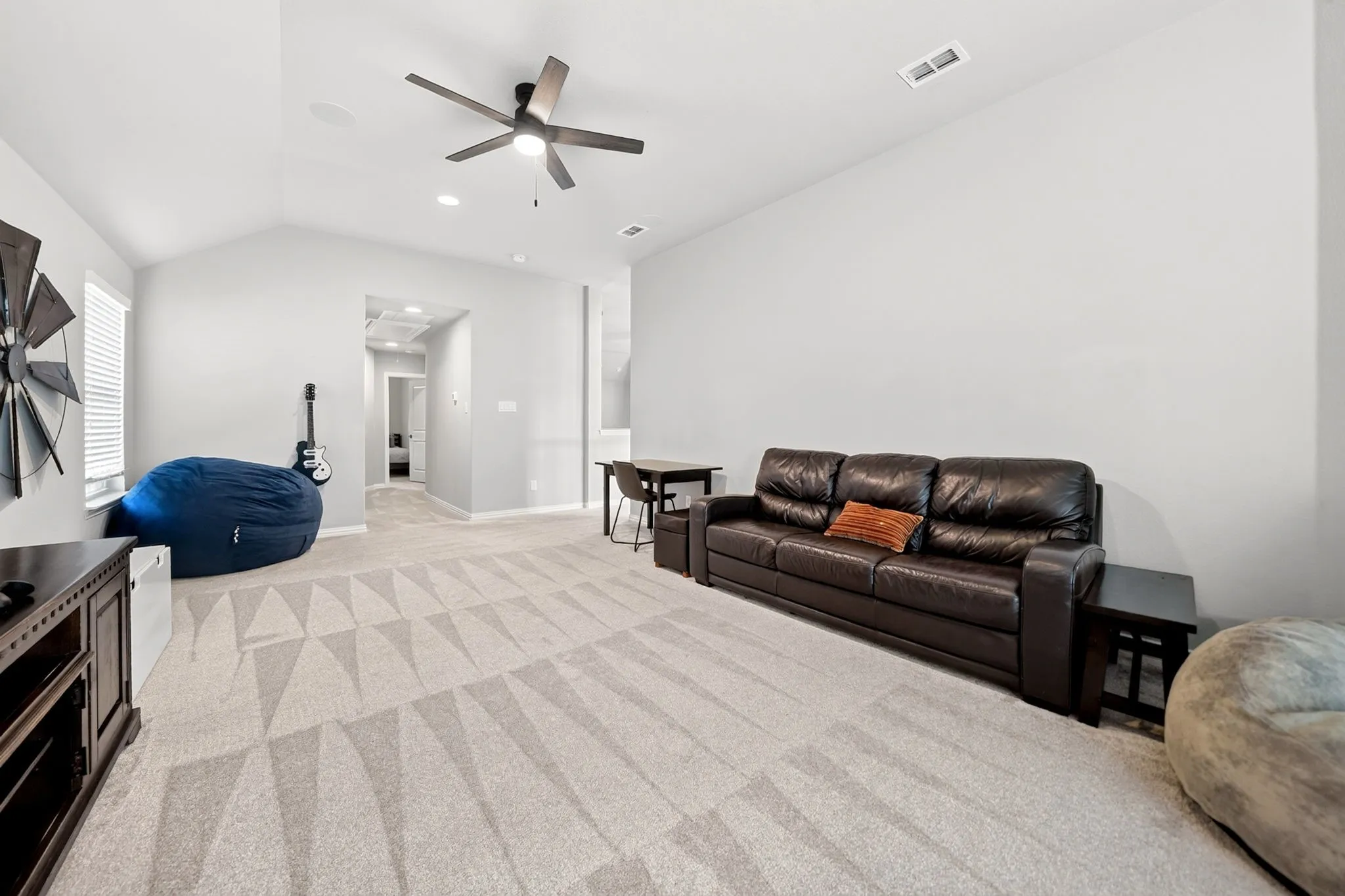 Spacious carpeted room featuring vaulted ceilings, a contemporary ceiling fan with integrated lighting, recessed lighting, and a window with blinds