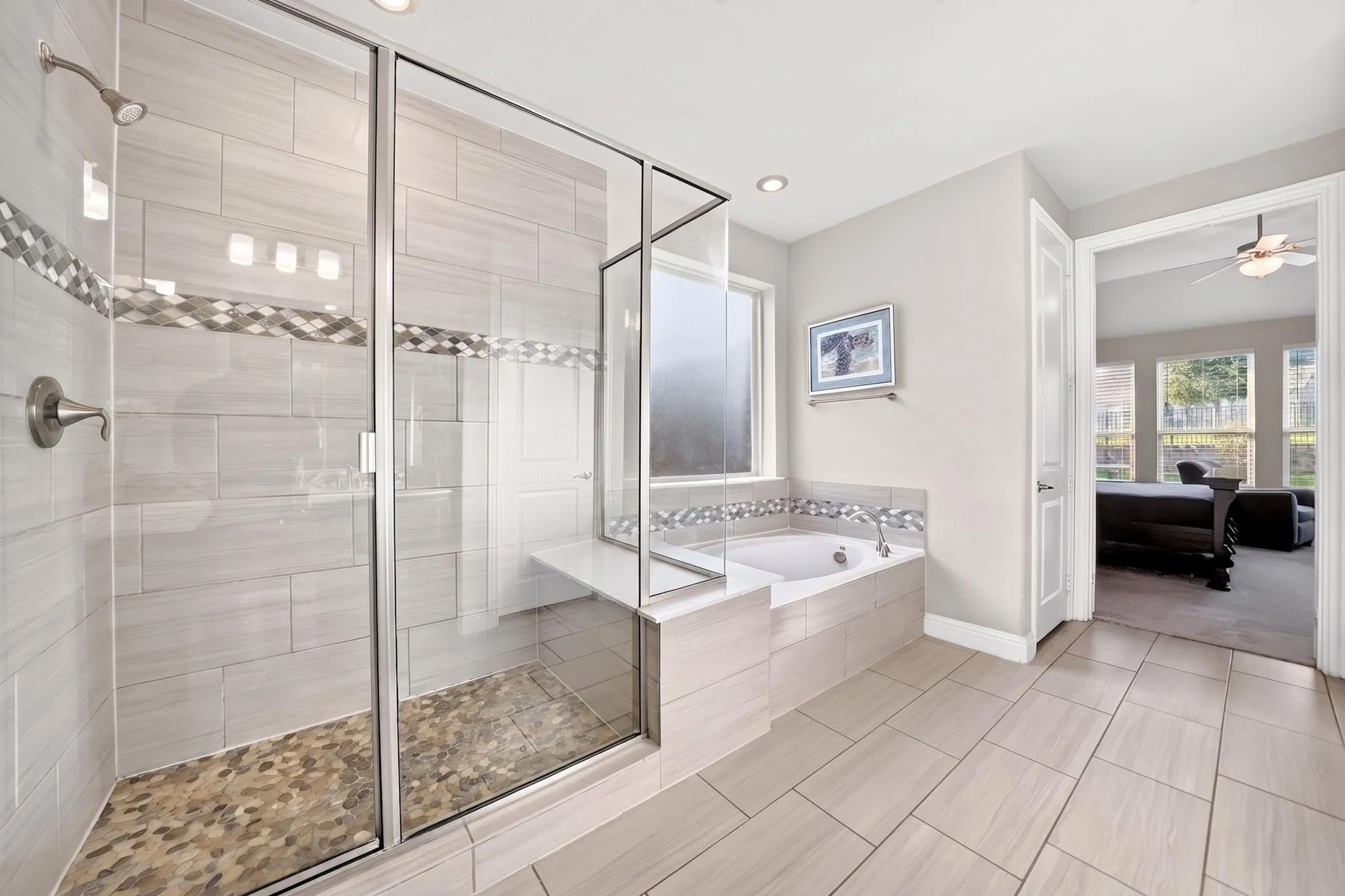 Bathroom featuring a glass-enclosed shower with pebble-tile flooring, a built-in tub with tile surround, and light-toned tile flooring