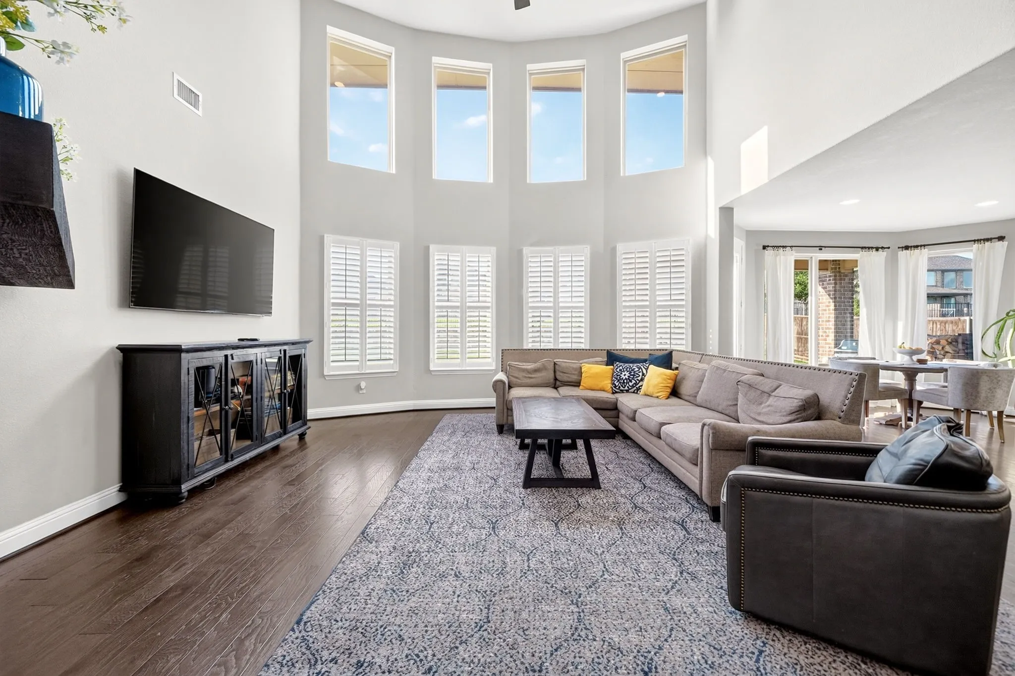 Two-story living area featuring tall windows with plantation shutters, wood-finish flooring, and light gray walls