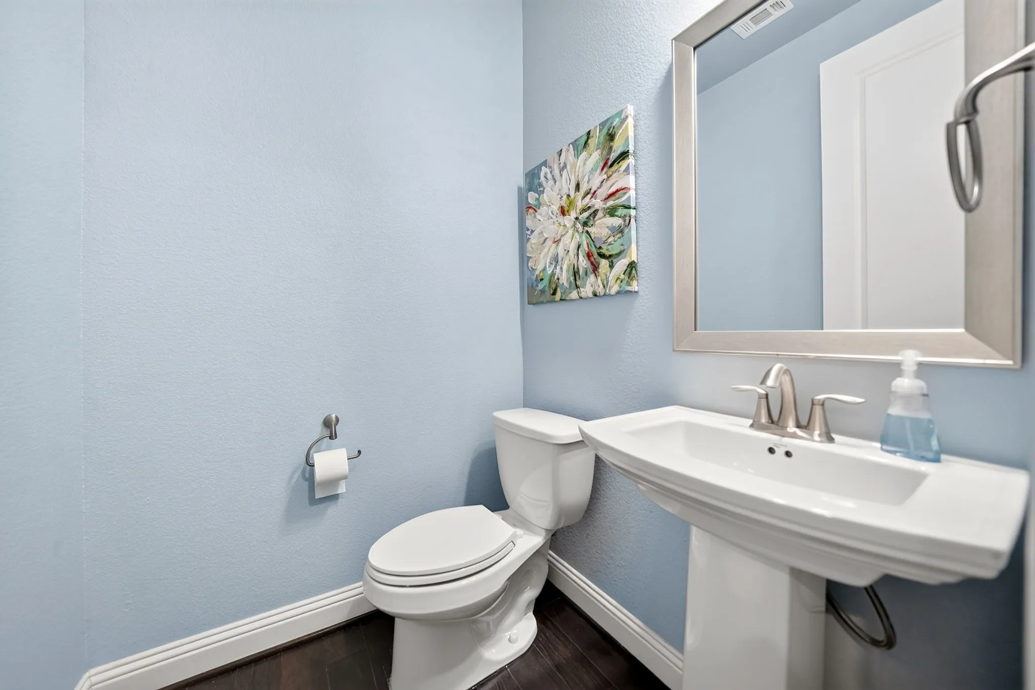 Pedestal sink with brushed nickel faucet, framed mirror, and dark wood-finish flooring