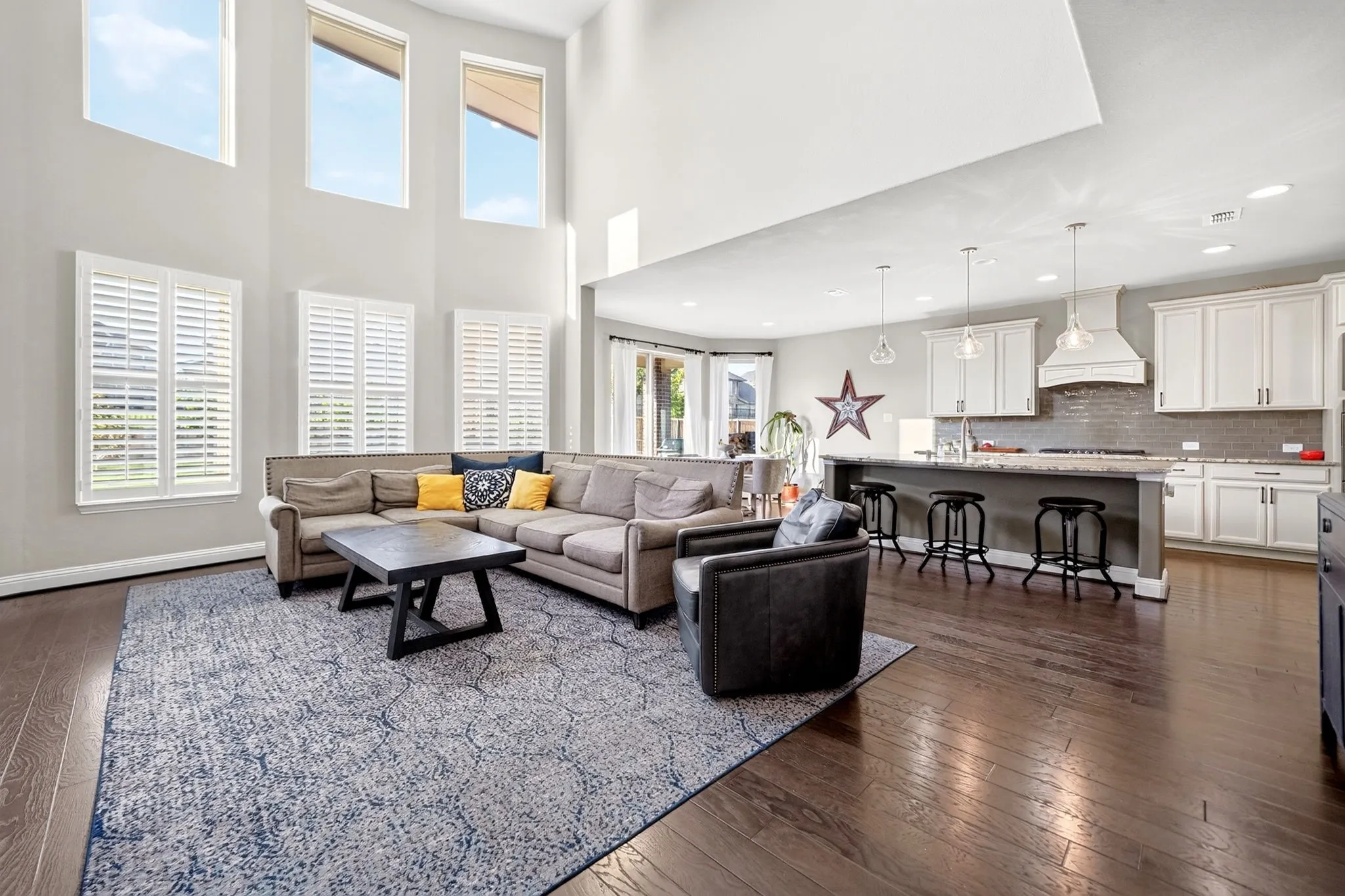 Open-concept living space featuring high ceilings, wood-finish flooring, and multiple windows with white plantation shutters