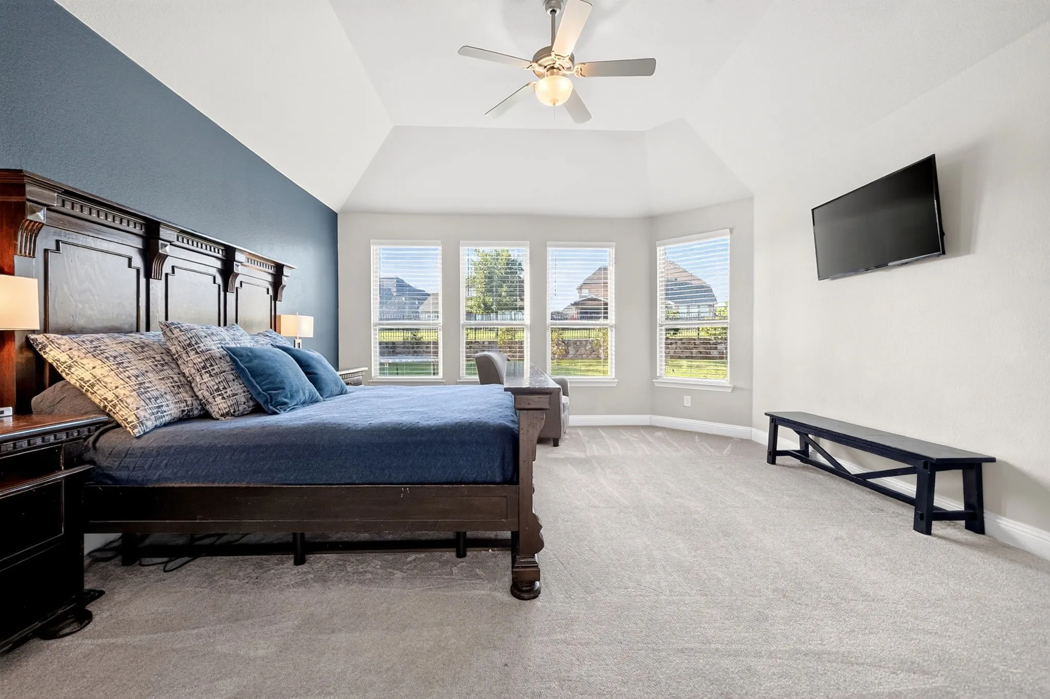 Spacious room featuring vaulted ceilings, bay windows, light-colored carpeting, a ceiling fan with integrated lighting, and a dark accent wall