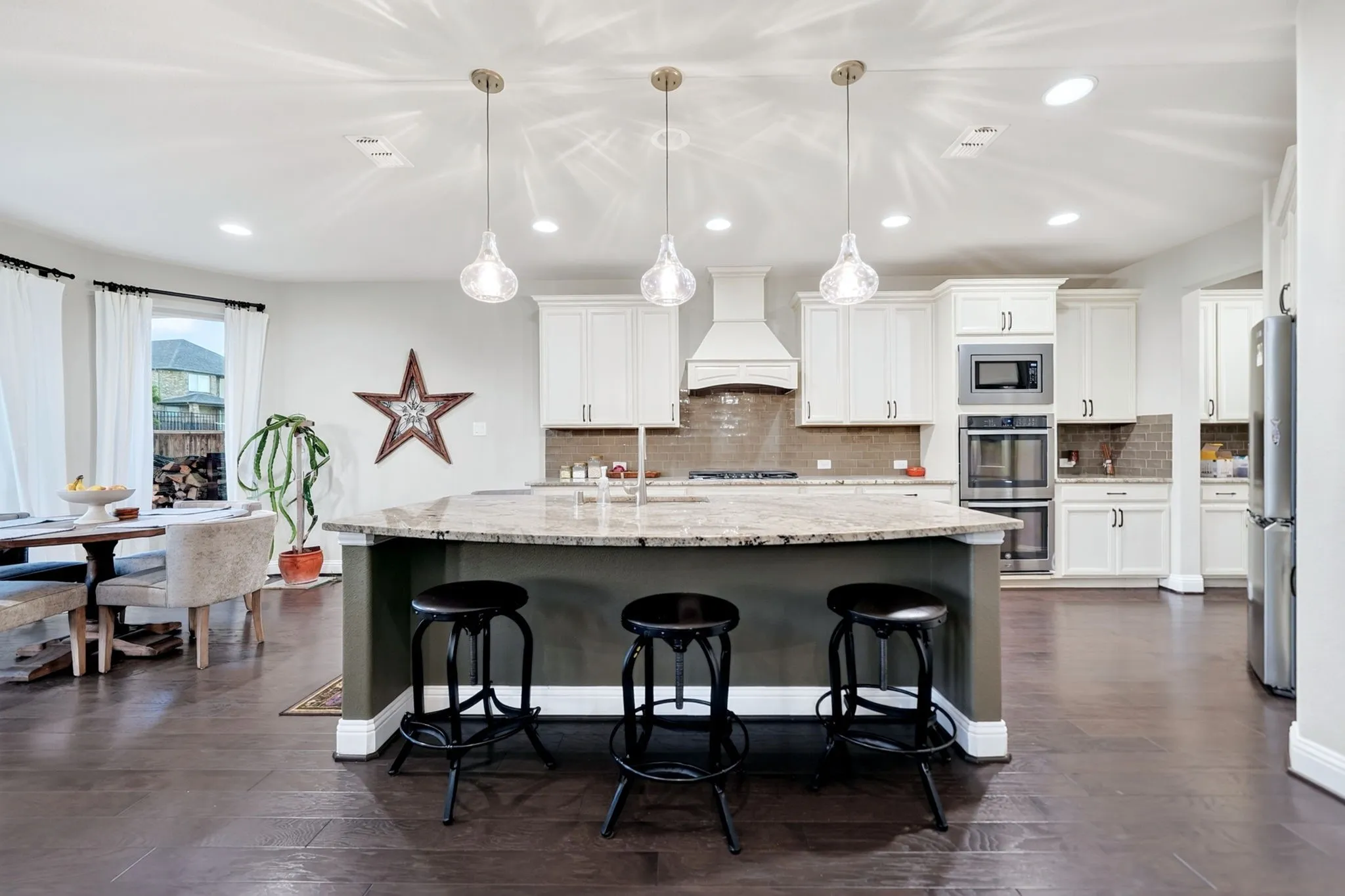 Kitchen featuring a large island with a stone countertop, pendant lighting, hardwood flooring, white cabinetry, and stainless steel built-in appliances