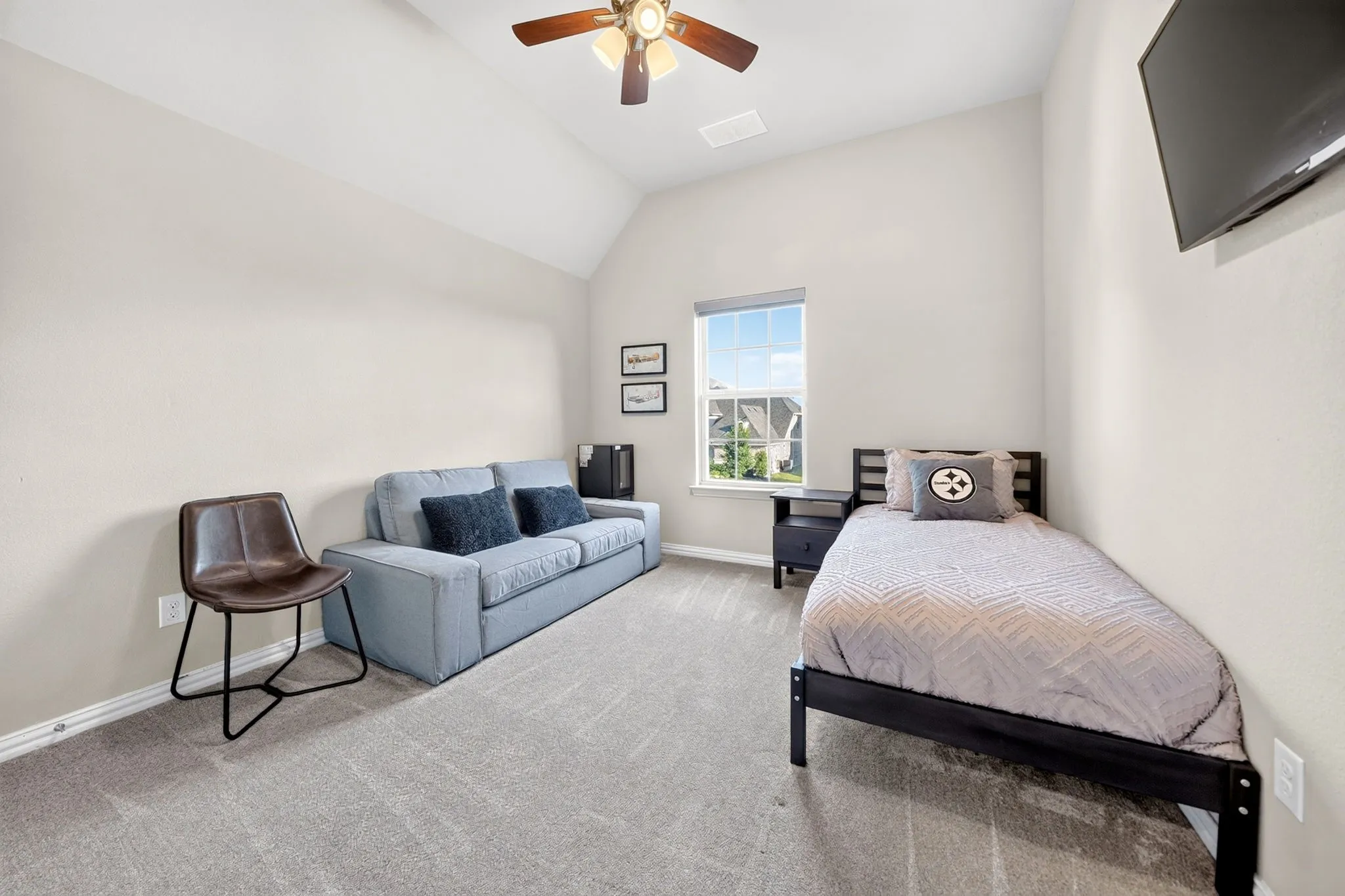 Carpeted room featuring a vaulted ceiling with a ceiling fan, a window, and a built-in wall-mounted television