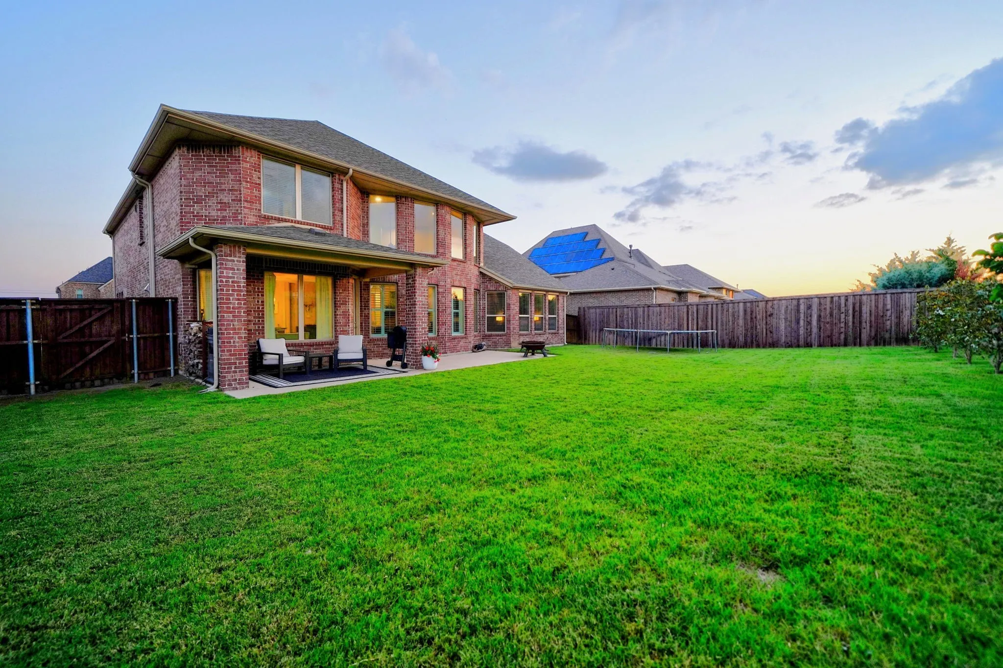 Spacious backyard featuring a large brick exterior home with multiple windows, a covered patio, and a wood privacy fence