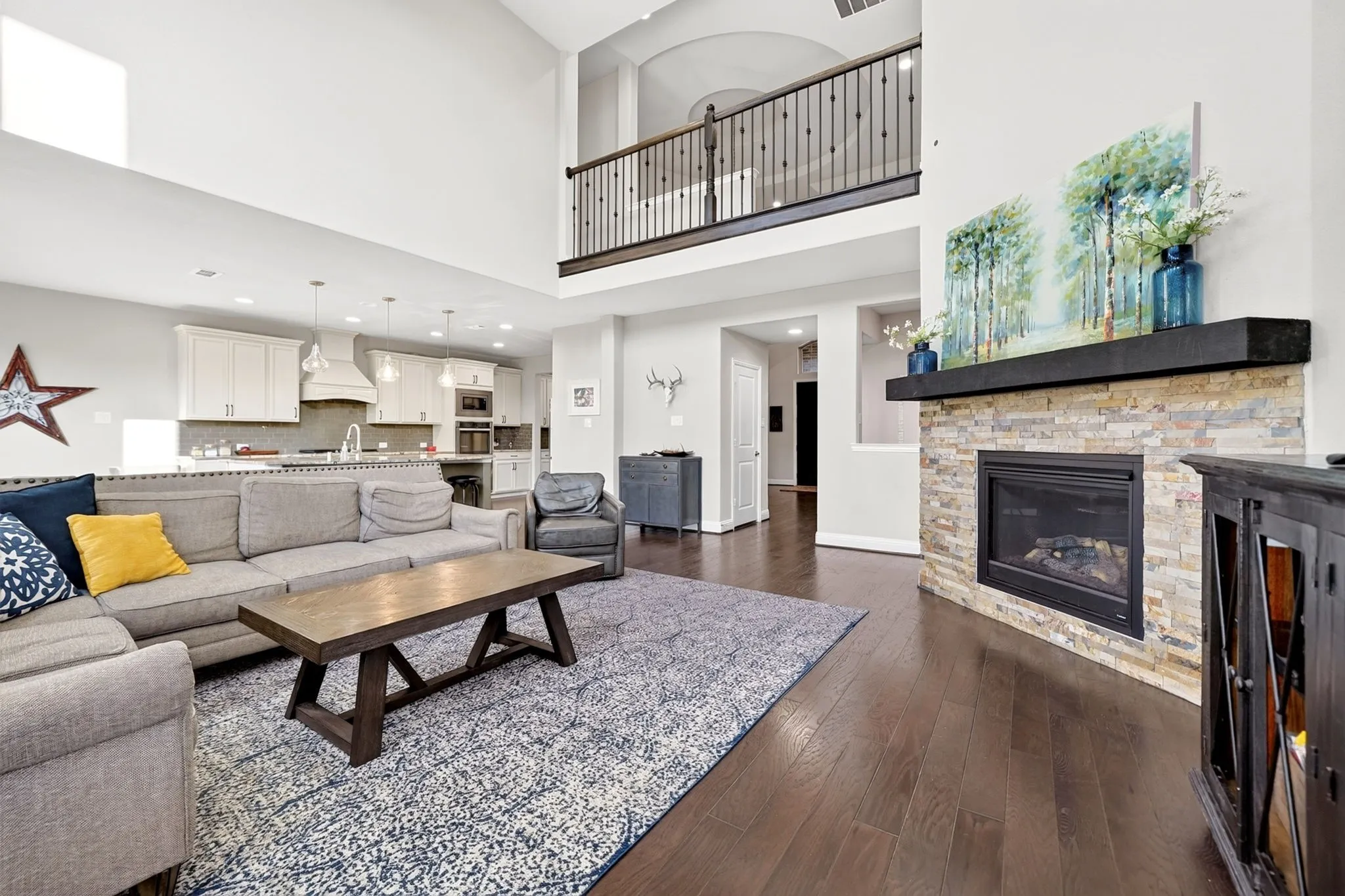 Open-concept living area with a stacked stone fireplace featuring a dark wood mantel