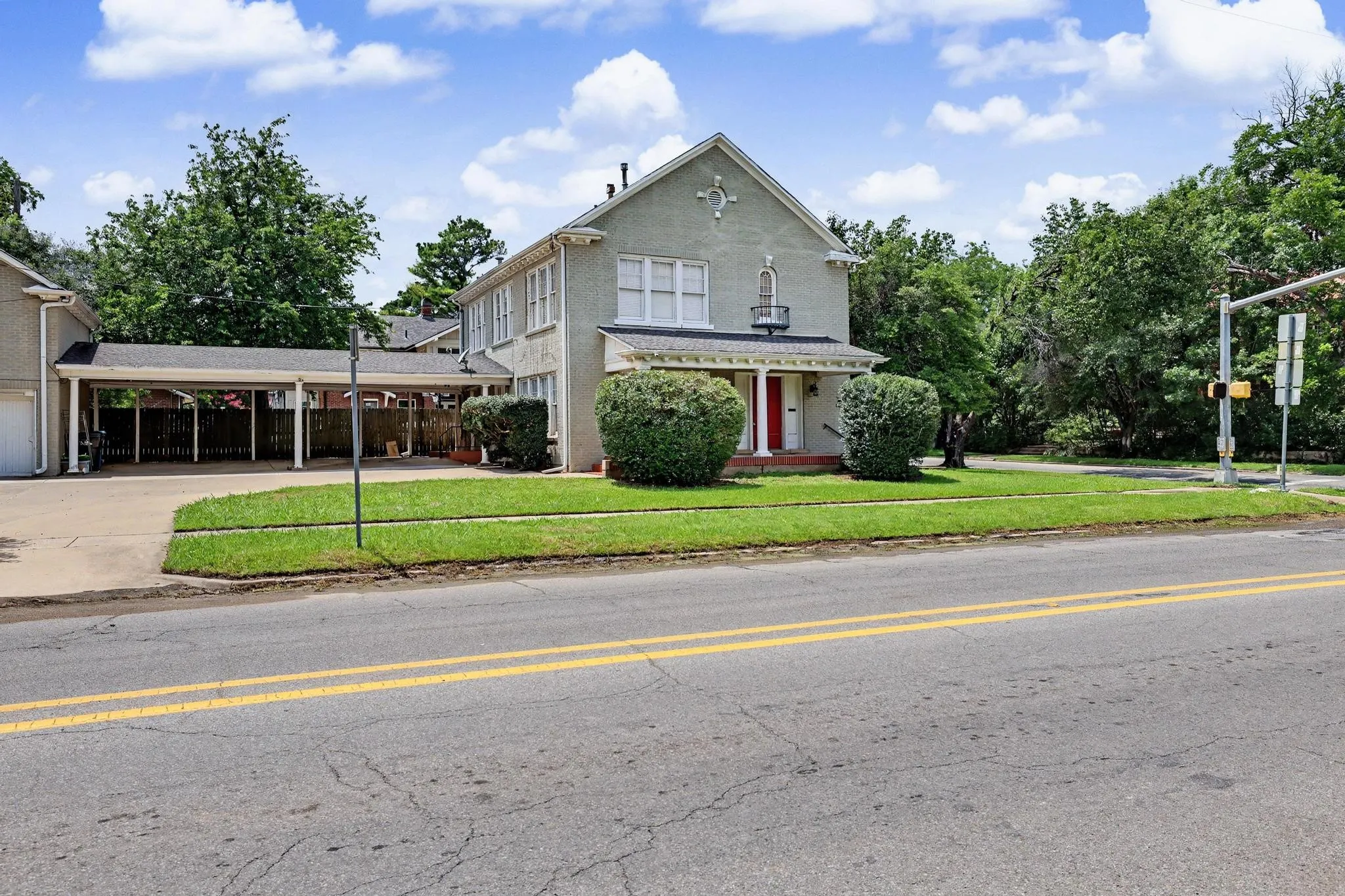 Multistory property featuring a light-colored stucco exterior, a covered carport, and a front porch with white columns