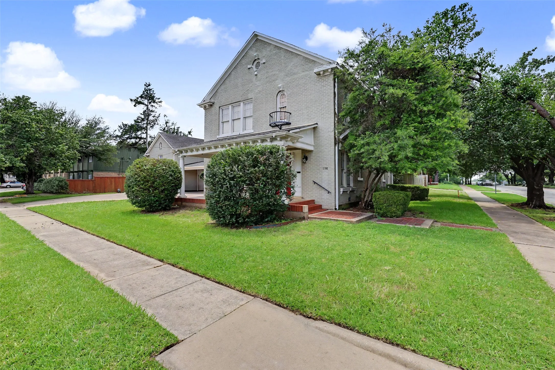 Traditional-style residence featuring a light-colored brick exterior, a covered porch entry, and mature landscaping