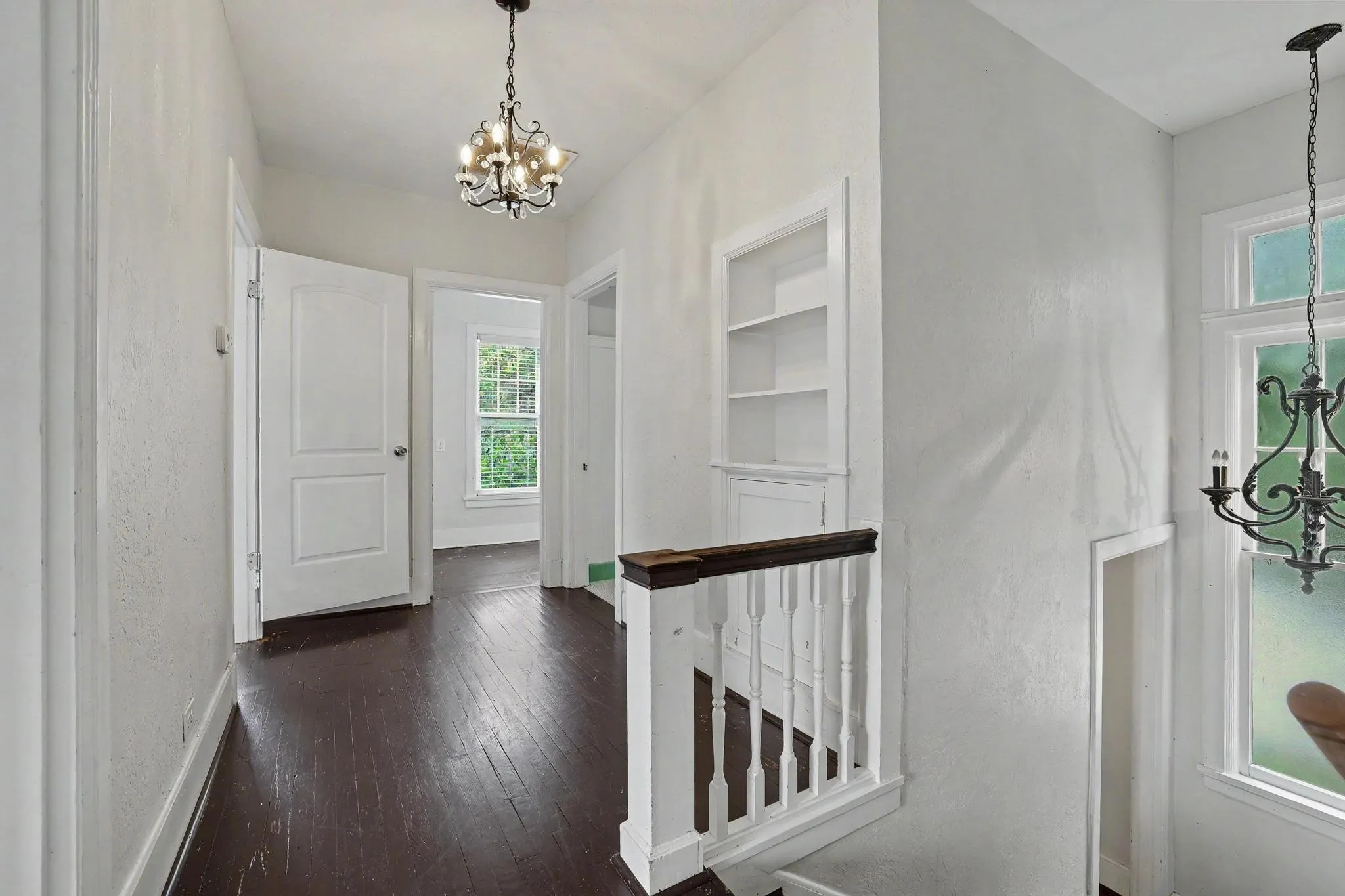 Hallway featuring dark wood-finish flooring, white walls, and a decorative chandelier