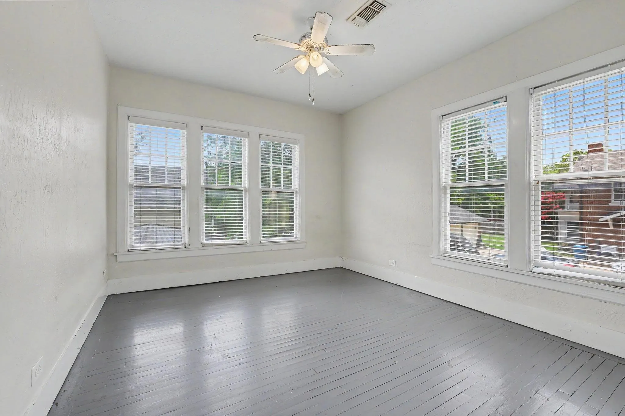 Room featuring painted wood flooring, multiple windows with blinds, a ceiling fan, and white walls