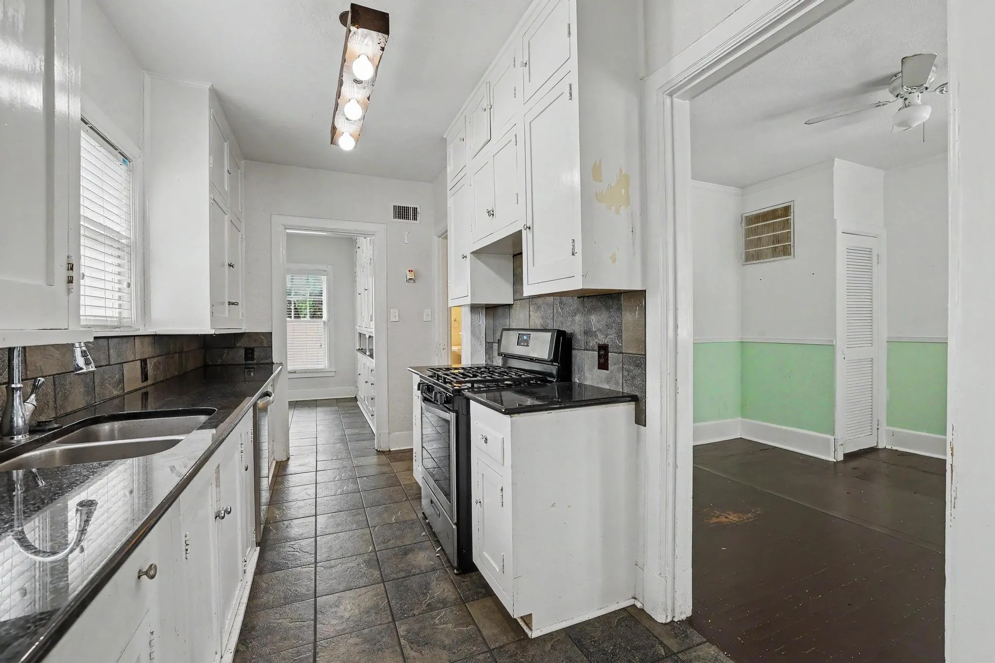 Galley kitchen featuring white cabinetry, dark countertops, a gas range, and tile flooring
