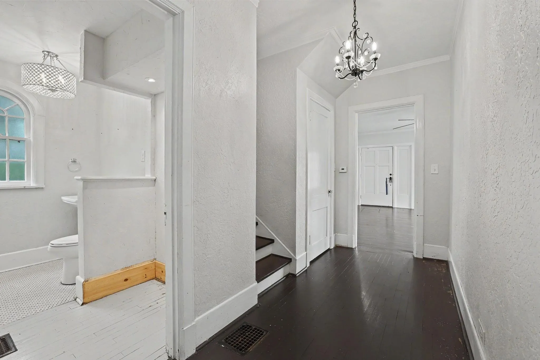 Hallway featuring dark wood-finish flooring, a decorative chandelier, white baseboards, and a doorway opening to a white-painted interior space