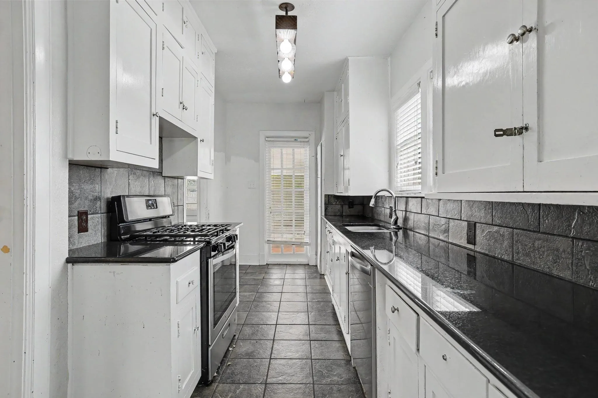 Galley kitchen featuring white cabinetry, dark countertops, tile flooring, a stainless steel gas range, and a glass-paned door