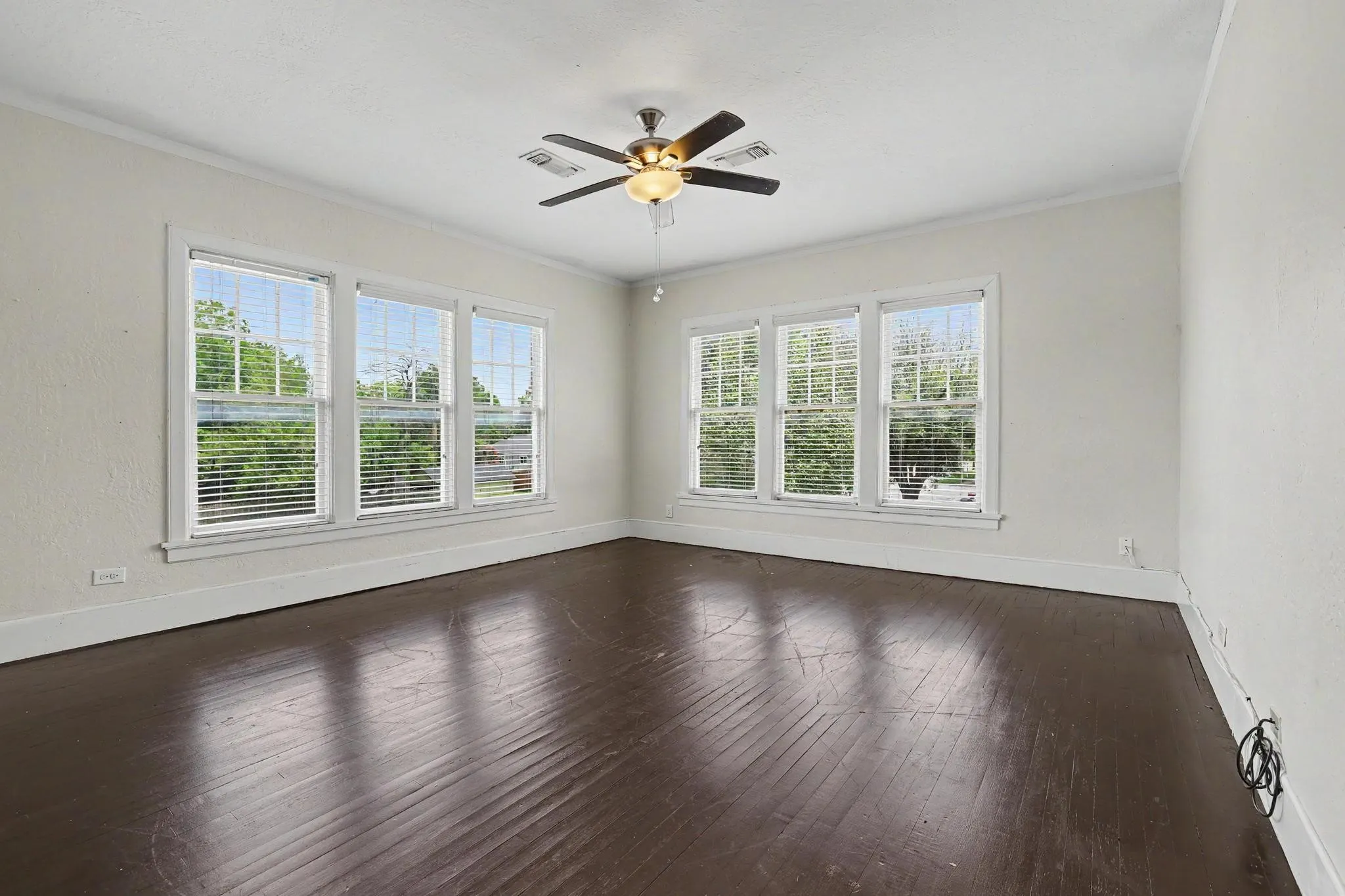 Spacious interior featuring dark wood-finish flooring, multiple windows with blinds, a ceiling fan with integrated lighting, white walls, and white trim molding