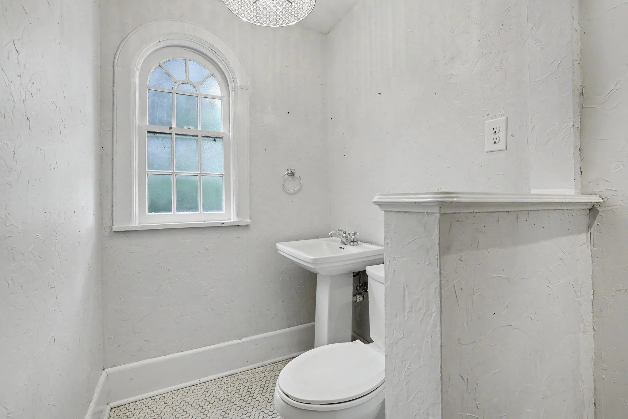 Bathroom featuring an arched window, pedestal sink, white fixtures, and mosaic tile flooring