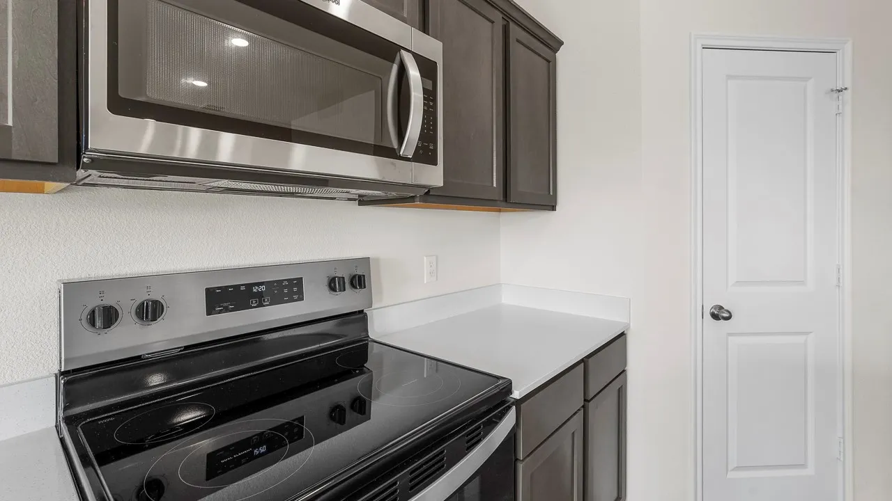 Modern kitchen featuring a stainless steel microwave, electric range with a ceramic cooktop, dark wood-finish cabinetry, and light-toned countertops