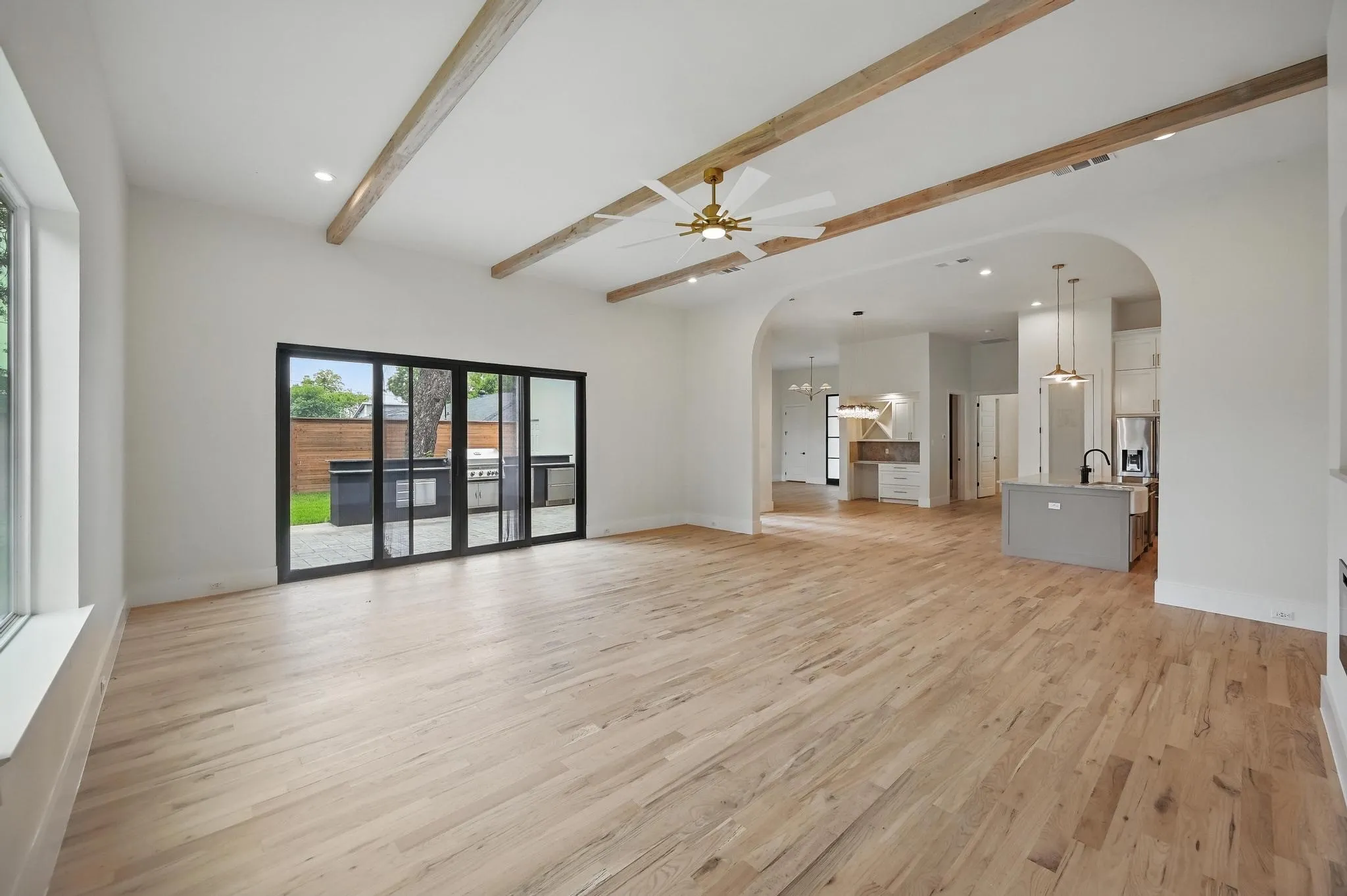 Expansive living area featuring wood-finish flooring, exposed ceiling beams, and a modern ceiling fan
