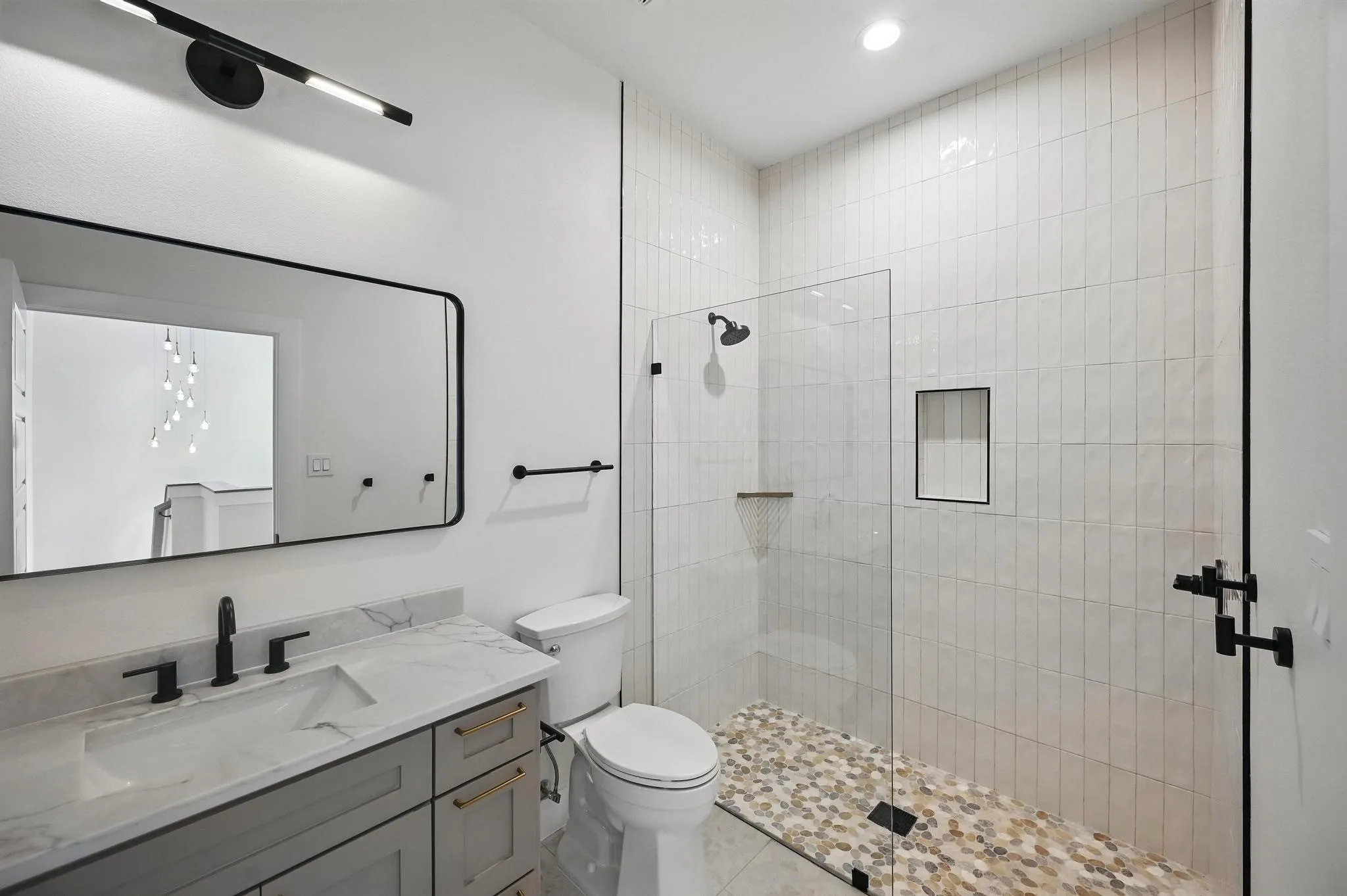 Modern bathroom featuring a glass-enclosed shower with pebble-style flooring and vertical subway tile