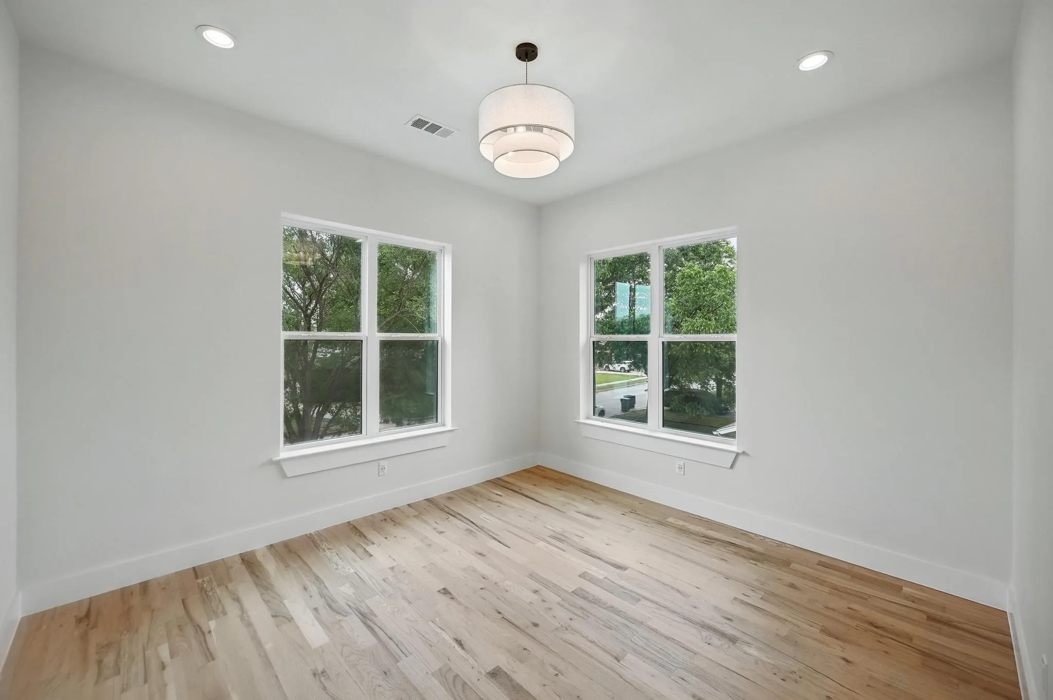 Bright interior space featuring wood-finish flooring, white walls, and a contemporary drum pendant light