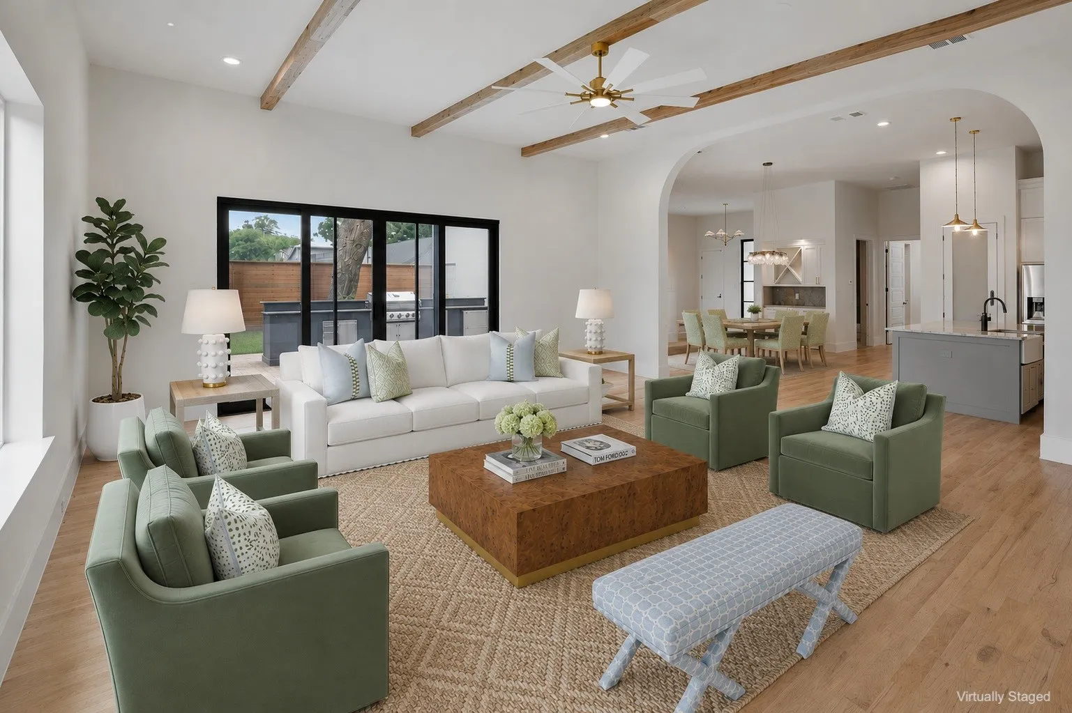 Spacious living area featuring exposed wood beams, a ceiling fan with integrated lighting, wood-finish flooring, and expansive black-framed sliding glass doors leading to an outdoor living space with built-in cabinetry