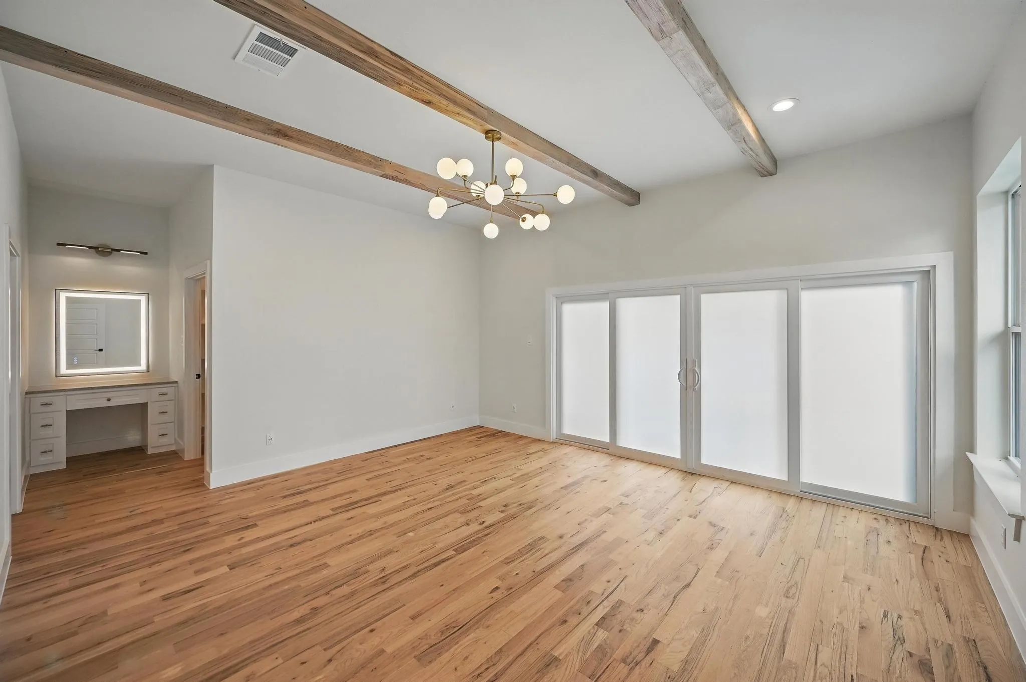 Spacious room featuring vaulted ceilings with exposed wood beams, wood-finish flooring, and a contemporary multi-bulb chandelier