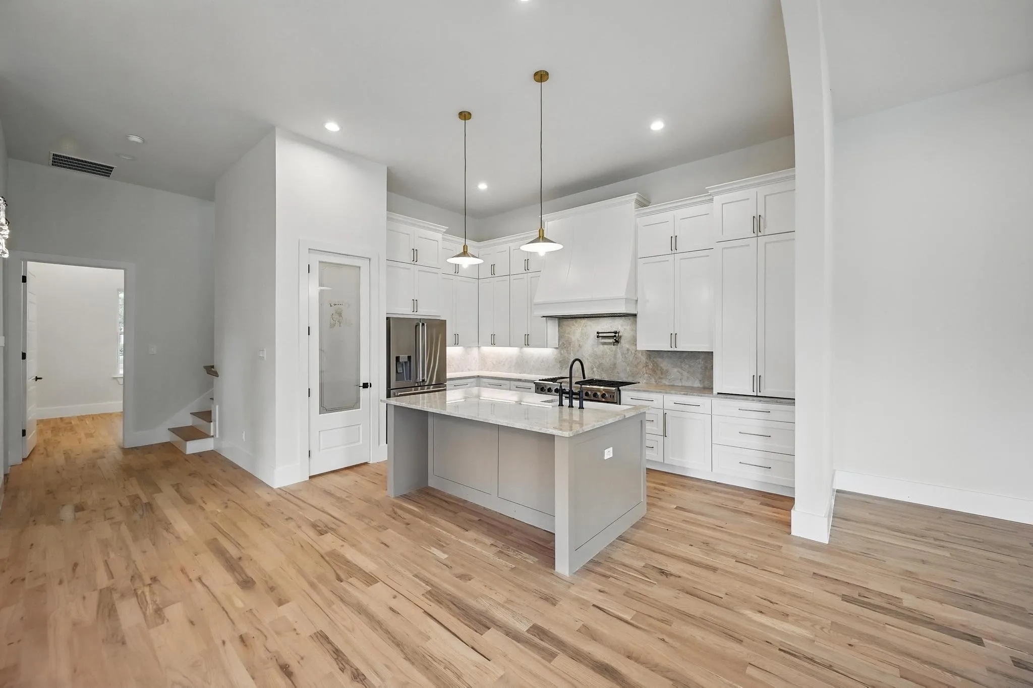 Gourmet kitchen featuring a central island with a light-toned countertop, white cabinetry with contemporary hardware, stainless steel appliances, and wood-finish flooring throughout