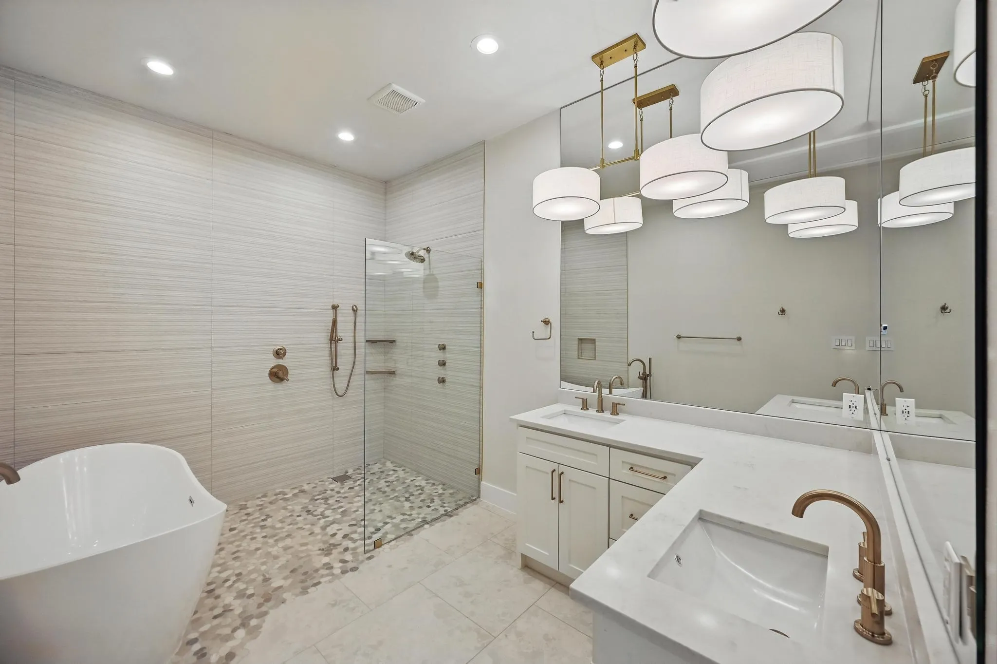 Contemporary bathroom featuring a freestanding soaking tub, a frameless glass shower enclosure with pebble-tiled flooring, and a dual vanity with undermount sinks