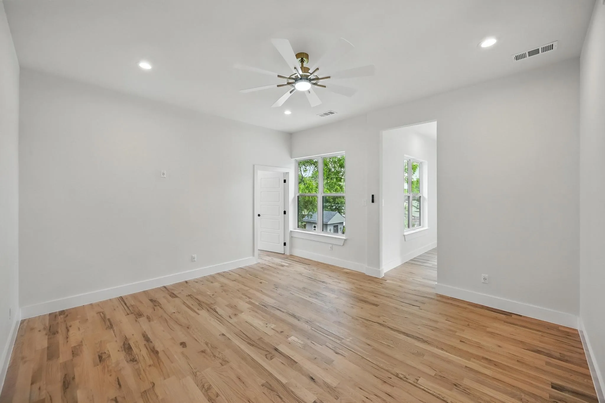Spacious room featuring wood-finish flooring, white walls, and a ceiling fan with integrated lighting