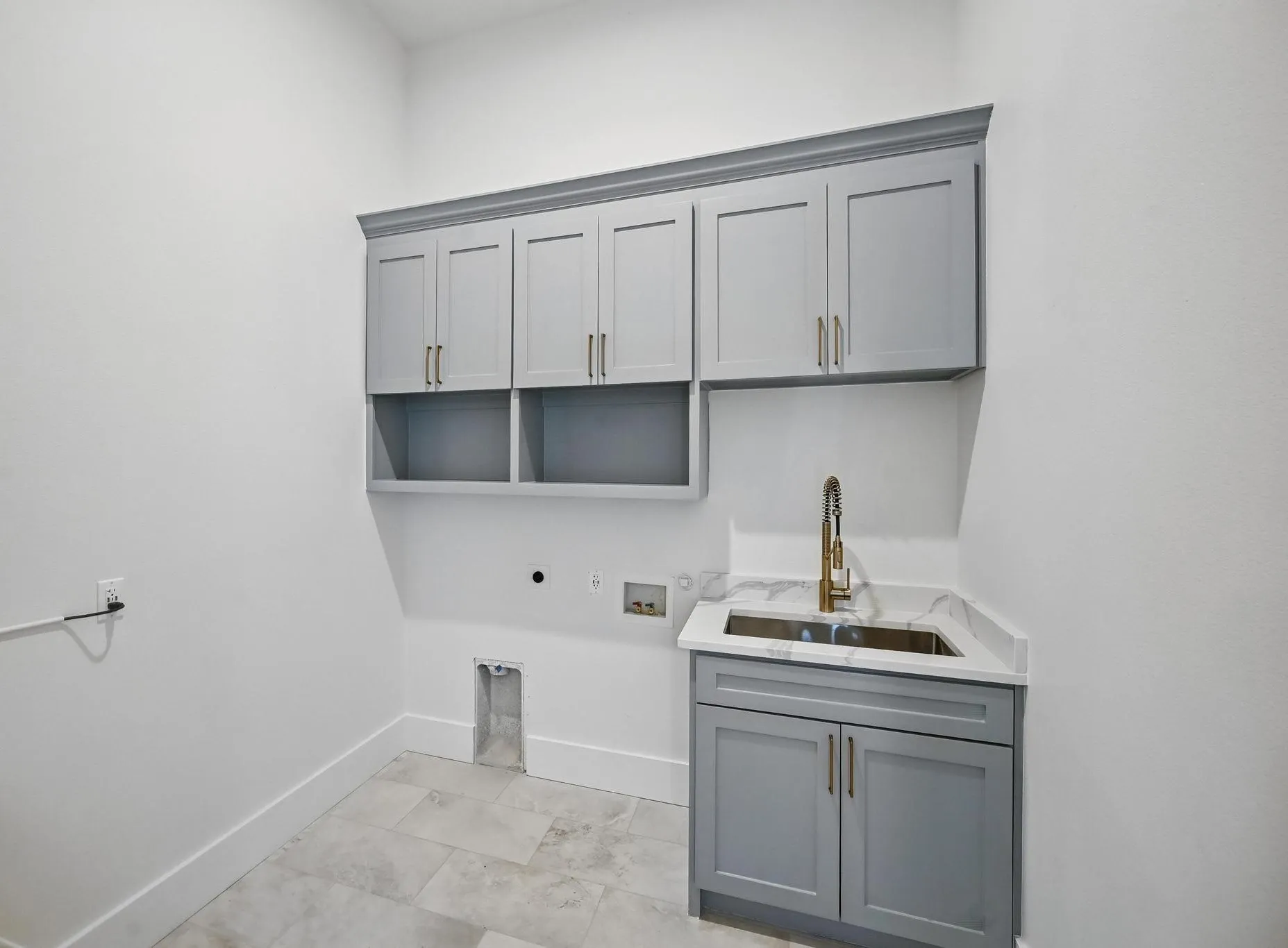 Utility room featuring light grey cabinetry with gold-finish hardware, a built-in sink with a gooseneck faucet, light-toned countertop, and tiled flooring