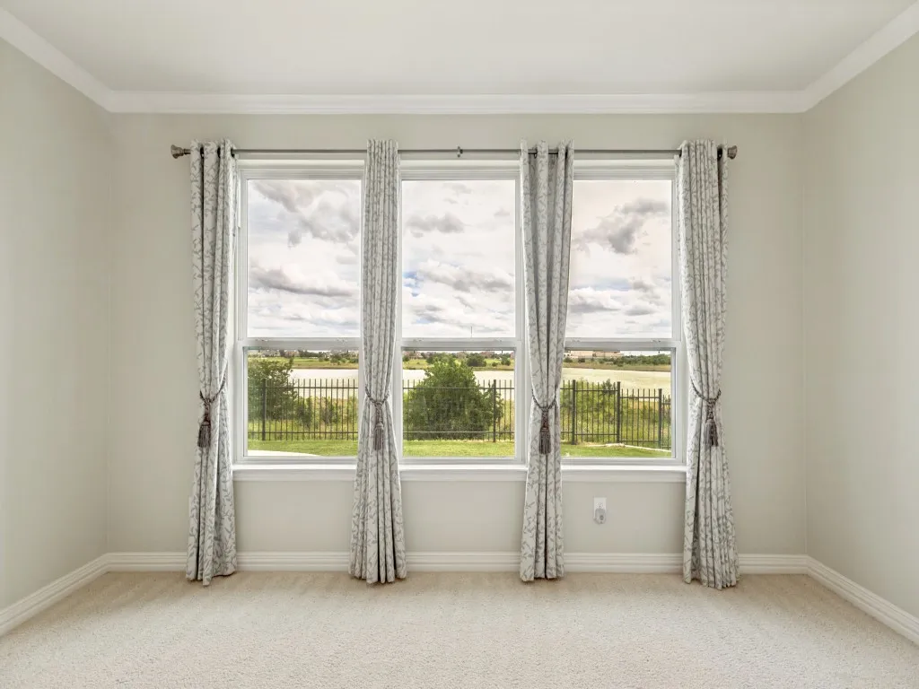 Wake up to this Lake View! Spacious Primary Bedroom featuring three large windows with curtain treatments, white crown molding, a ceiling fan with integrated lighting, and neutral-toned carpeting.