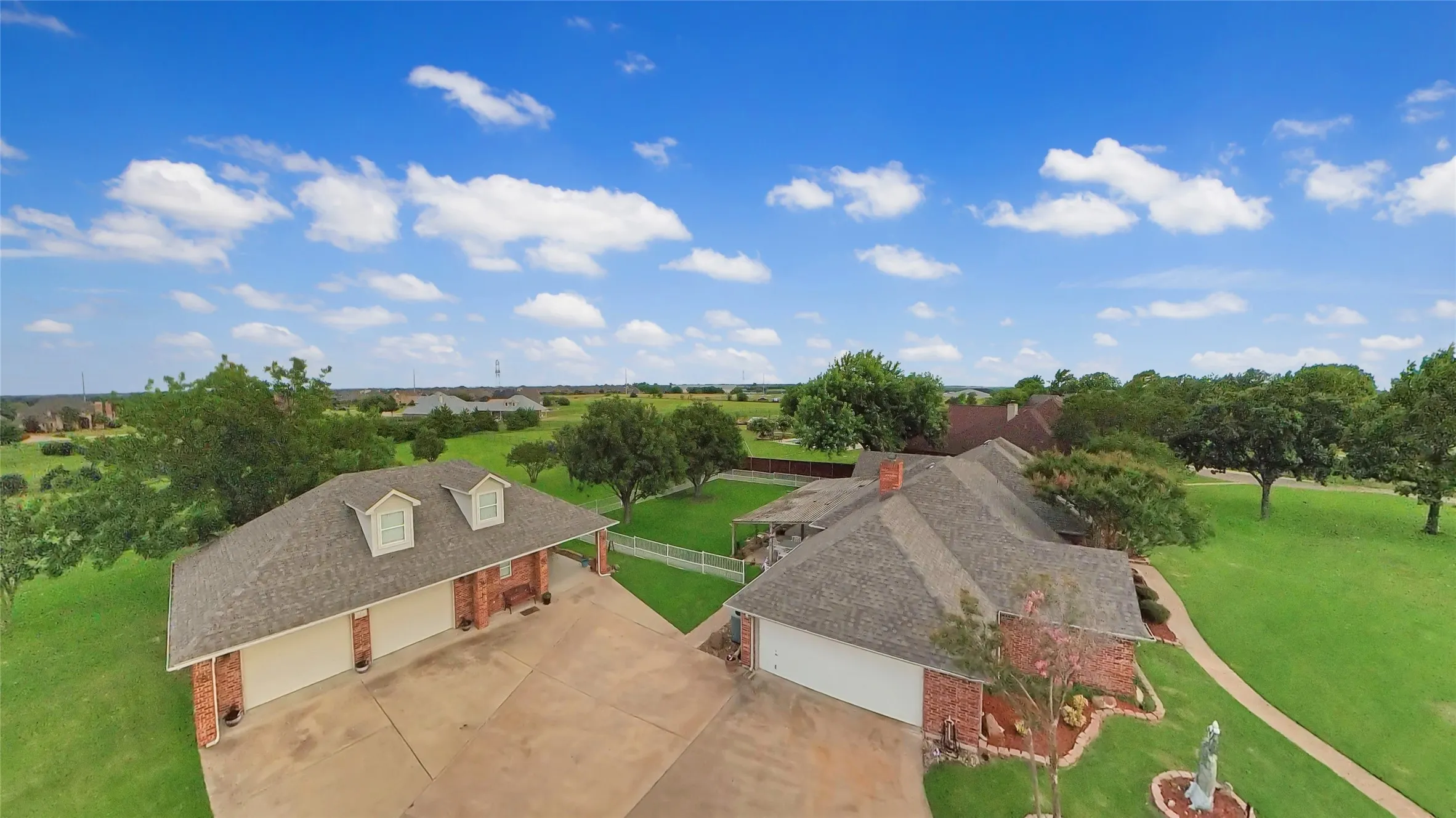 Expansive property featuring two distinct brick structures with shingle roofs and multiple garage doors