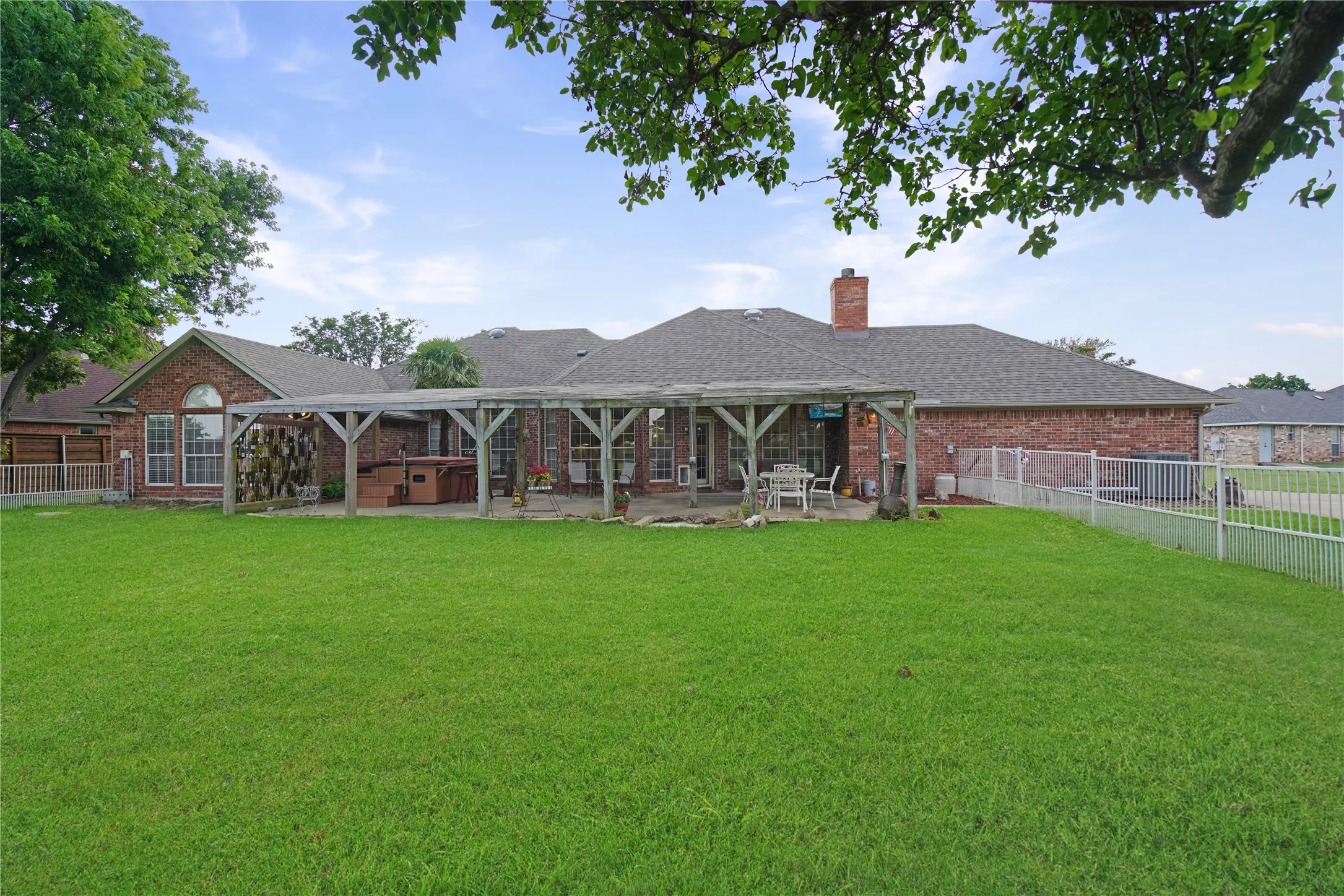 Expansive backyard featuring a lush lawn, a full brick exterior, a covered patio with a pergola, and a brick chimney