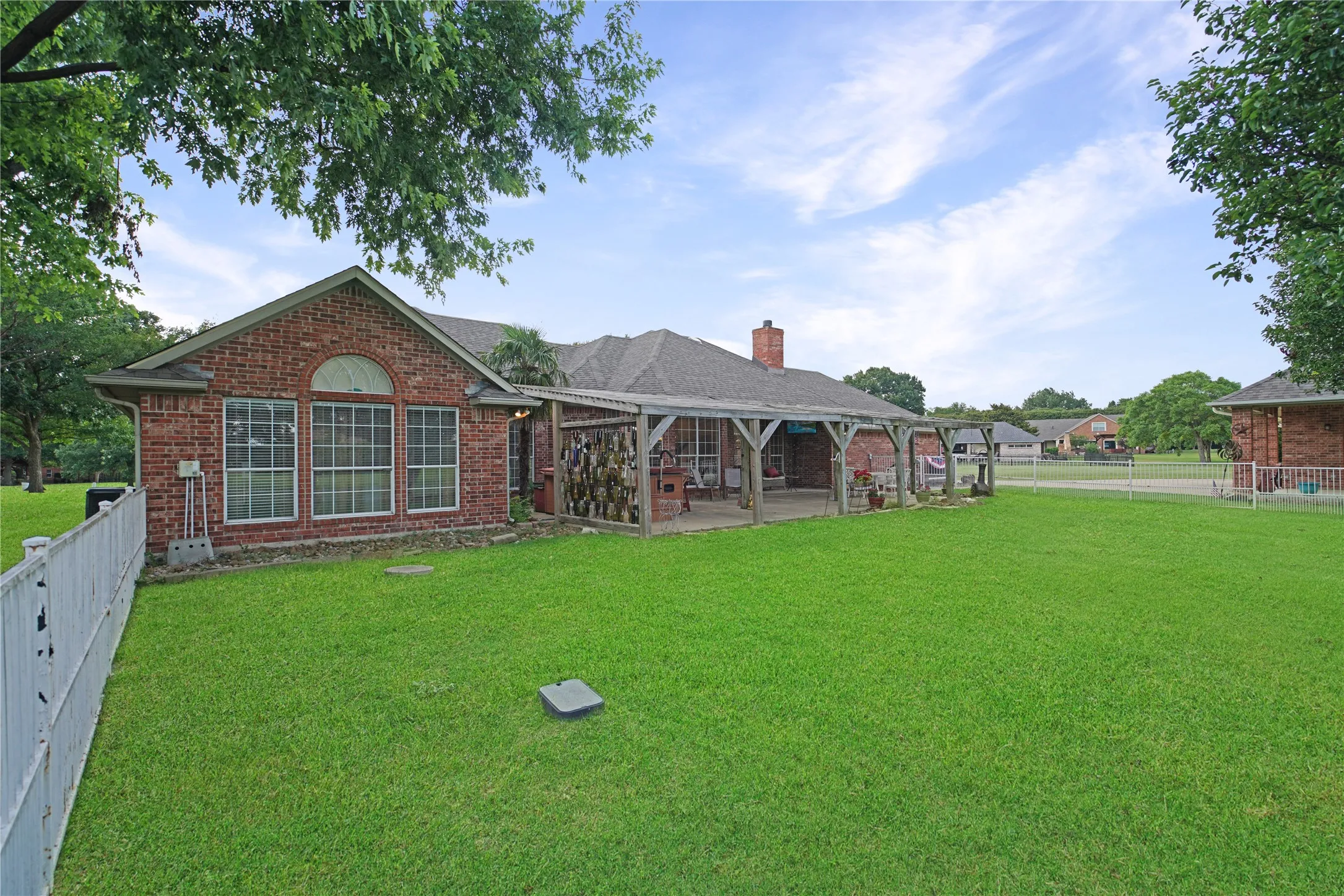 Expansive green lawn with a white picket fence, featuring a brick exterior with multiple windows and an arched transom window