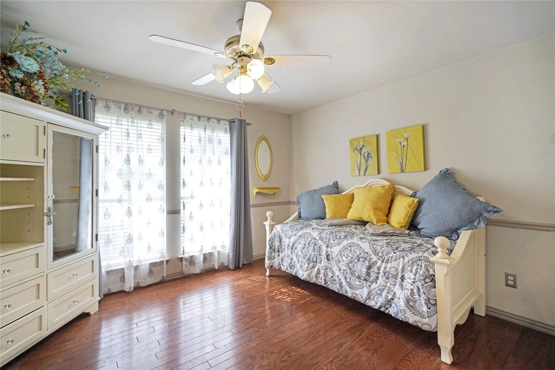 Hardwood-style flooring throughout this space with a ceiling fan light fixture and two windows featuring blinds and curtains