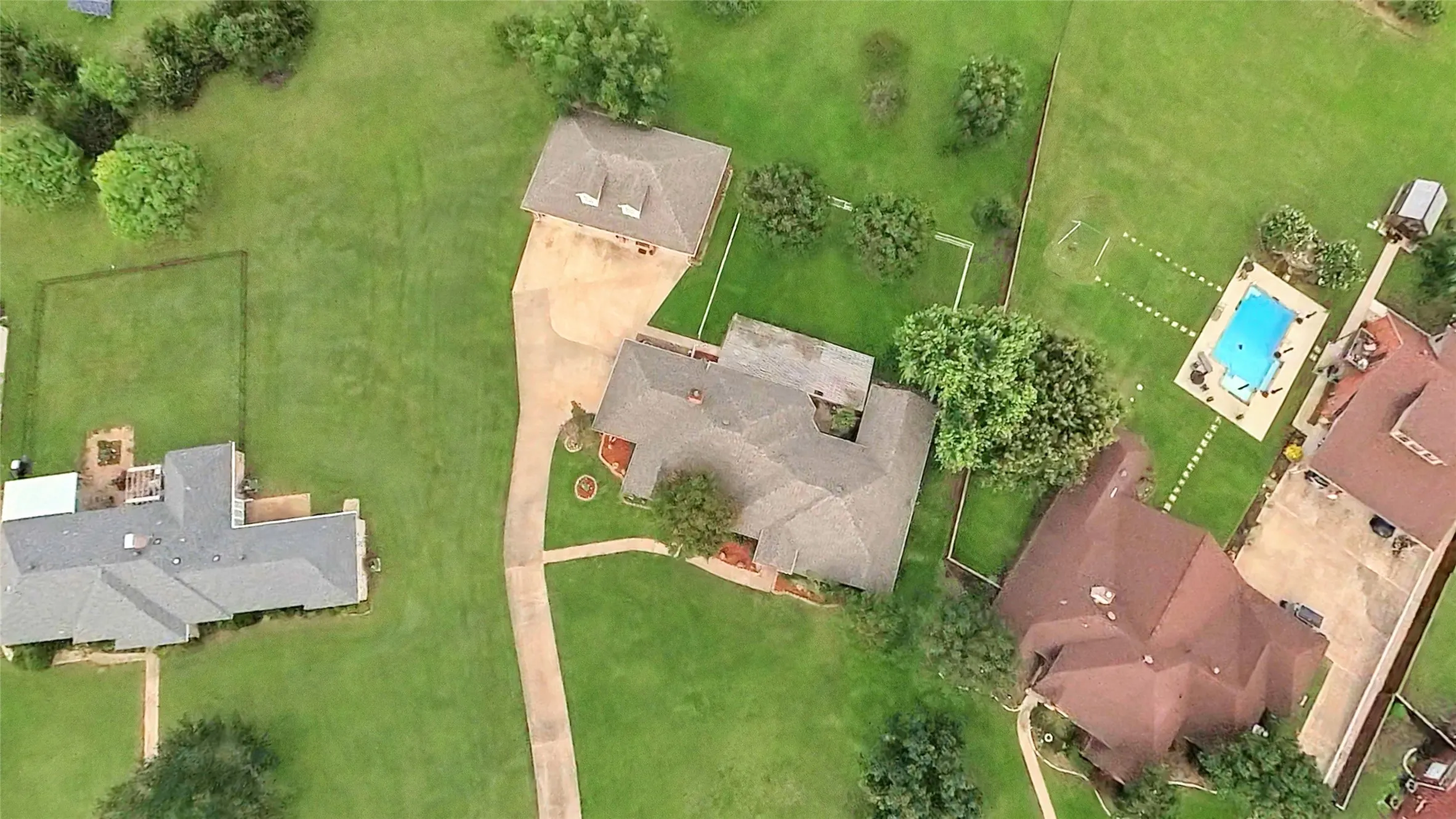 Expansive property featuring a main residence with a gabled roof, an auxiliary structure with a gabled roof, a substantial driveway, and ample green space