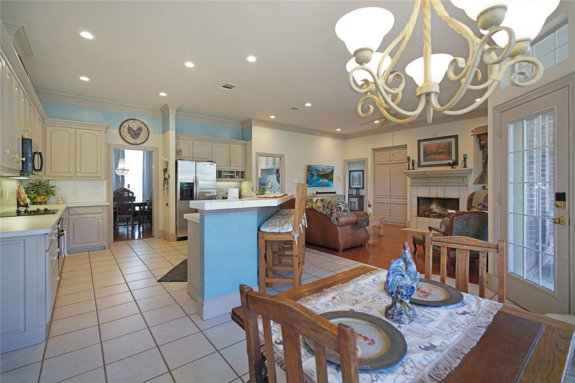 Open-concept kitchen and living area featuring tile flooring, white cabinetry, a built-in breakfast bar, a fireplace with a tile surround, and a glass-paneled exterior door