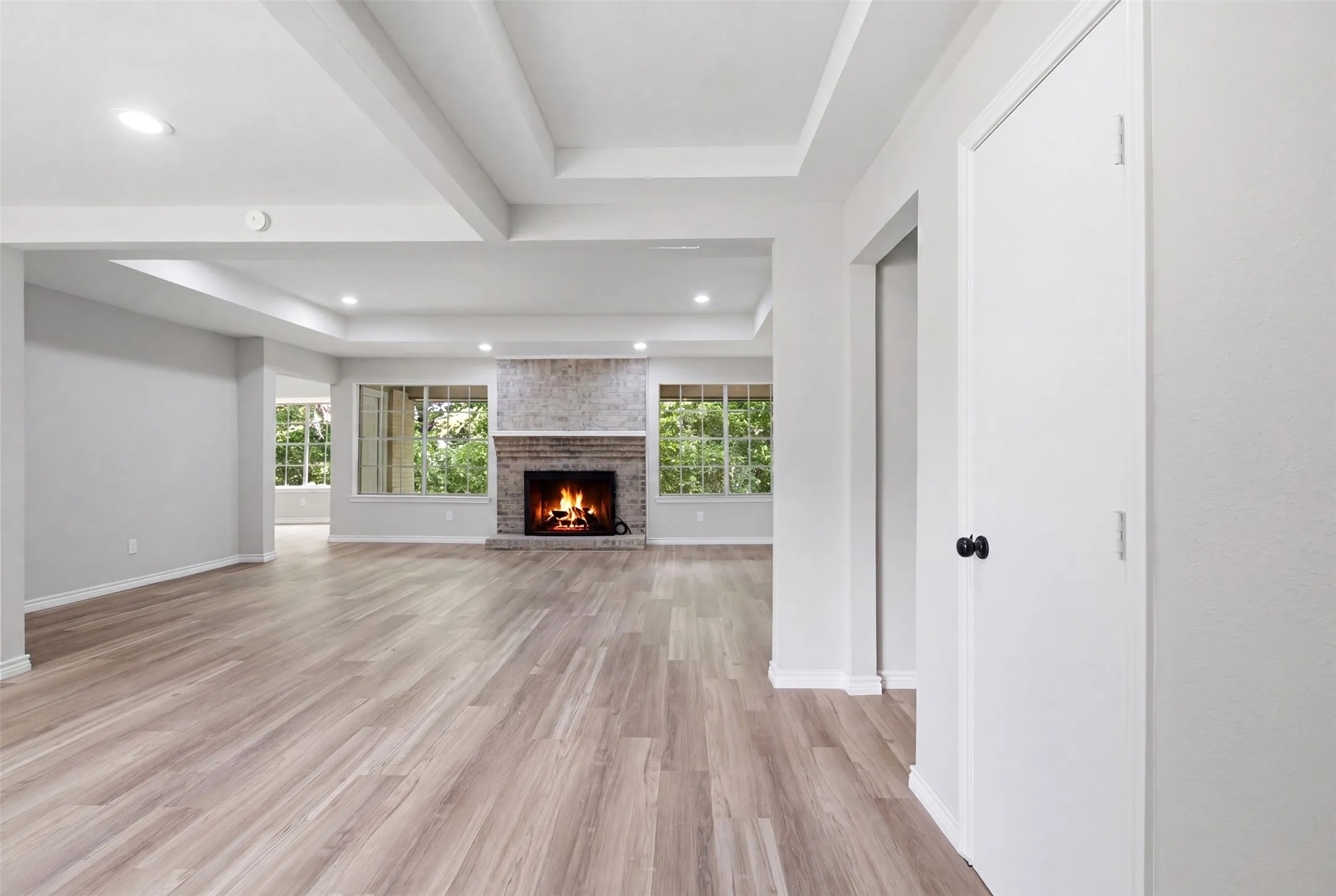Spacious interior with wood-finish flooring, a brick fireplace, tray ceiling detail, recessed lighting, and multiple windows